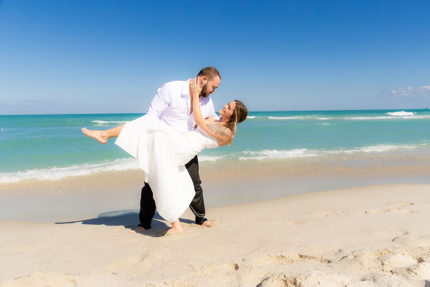Couple embraces on a scenic beach with crystal blue waters and white sand during a romantic photoshoot.
