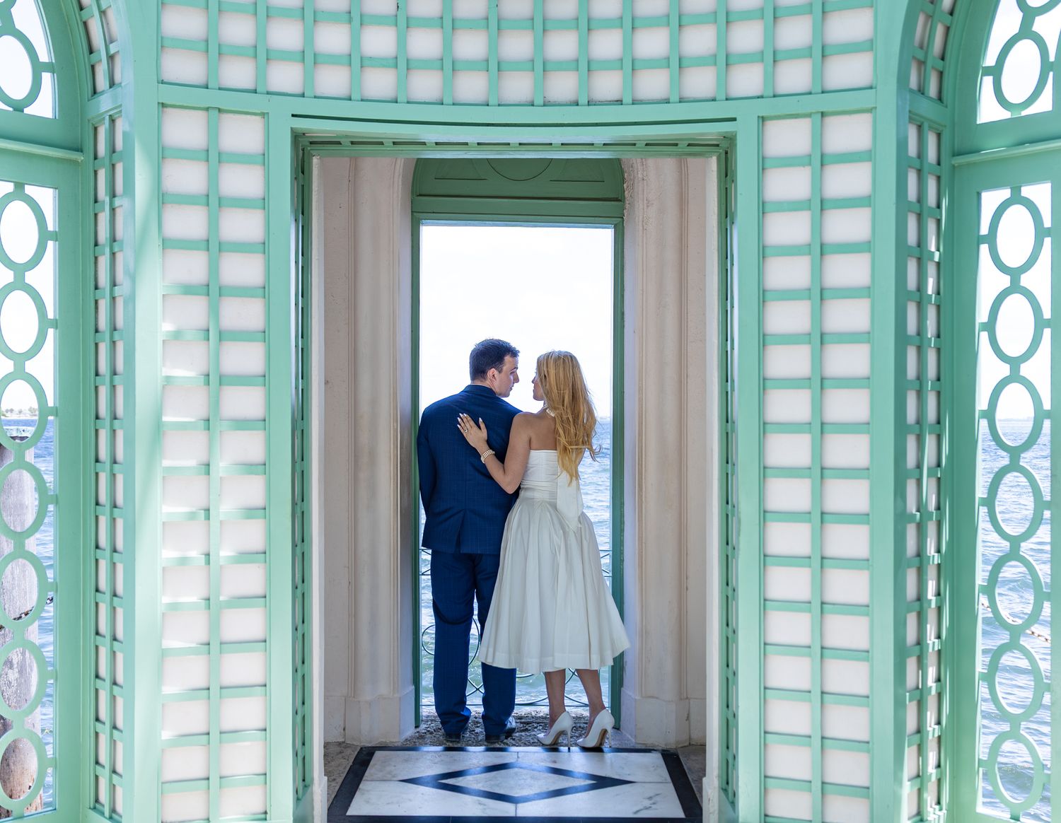 A couple stands in a mint-green gazebo's doorway with checkered floor tiles.