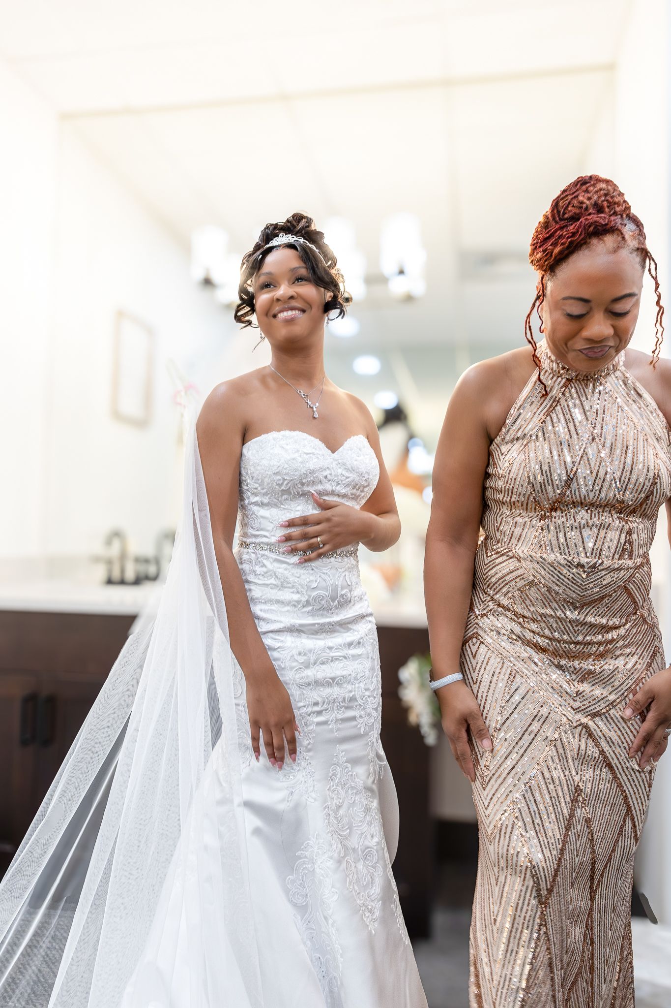 A bride in a white lace gown poses with mother in a sequined dress.