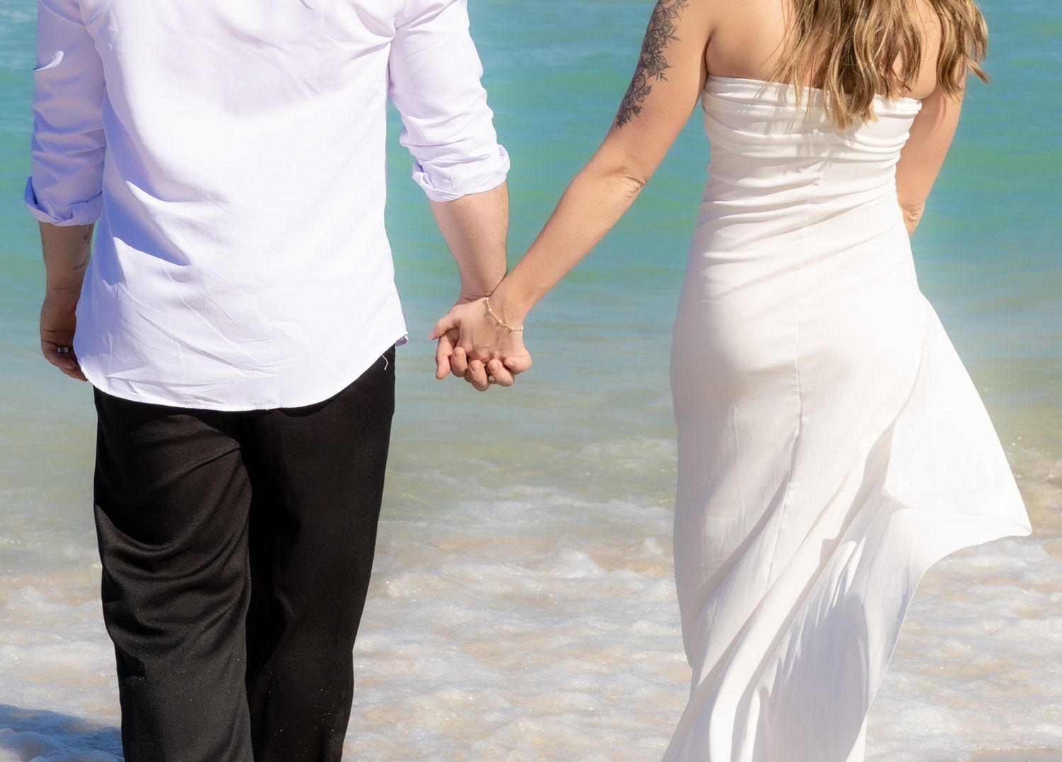 Couple walking hand in hand on a tropical beach with turquoise waters and white sand in the background.