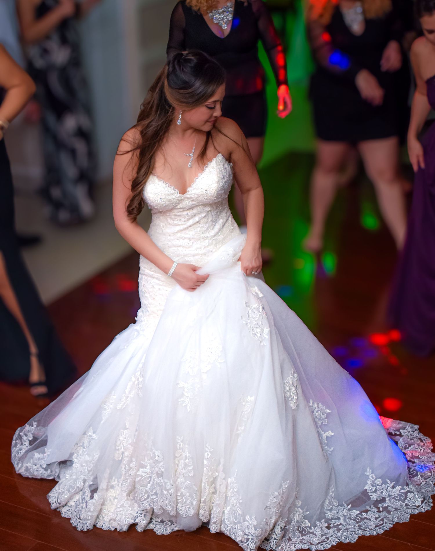 Bride wearing stunning white lace ballgown twirls on colorfully lit dance floor.