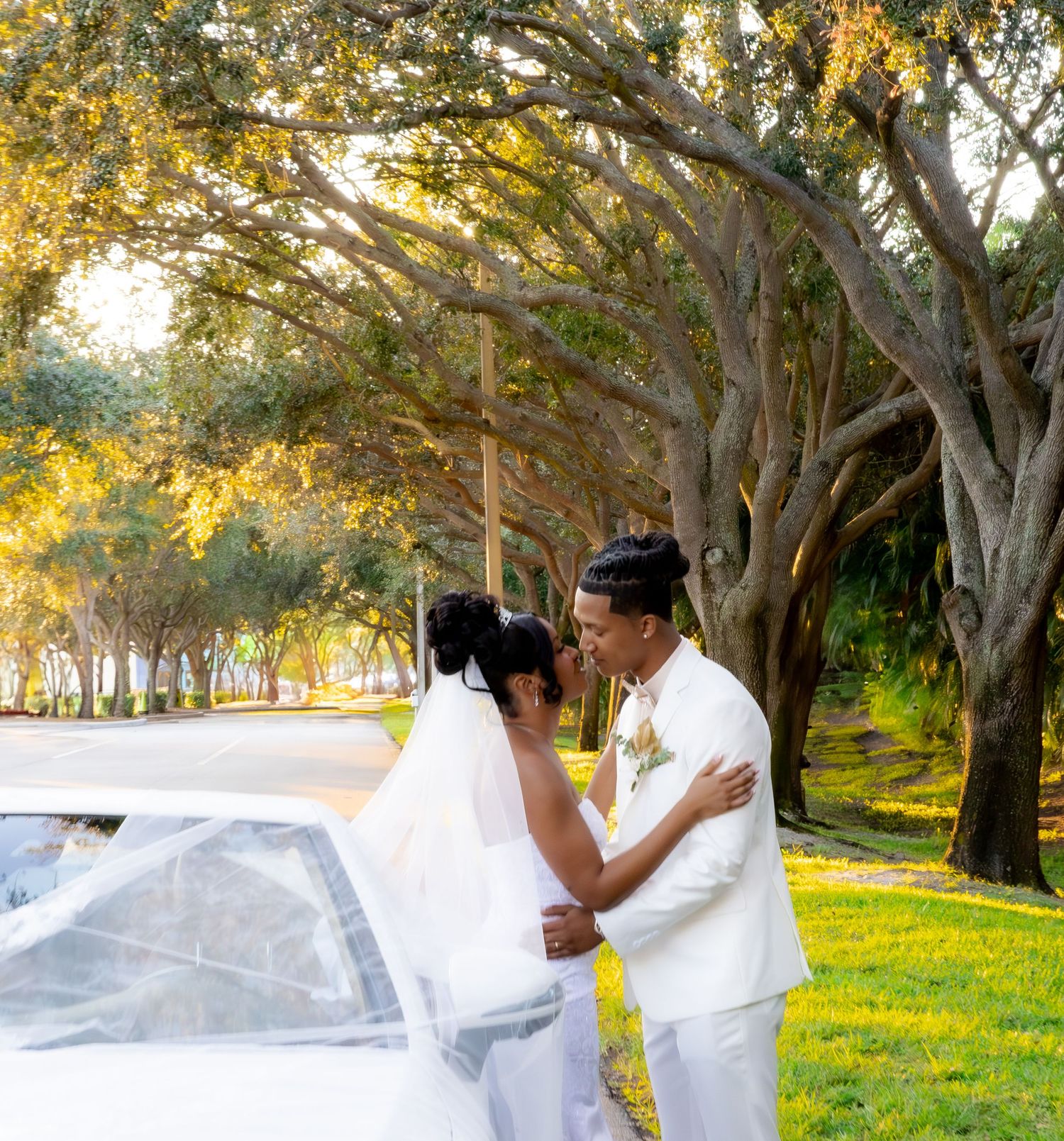 A romantic moment between newlyweds near their wedding car under golden trees.