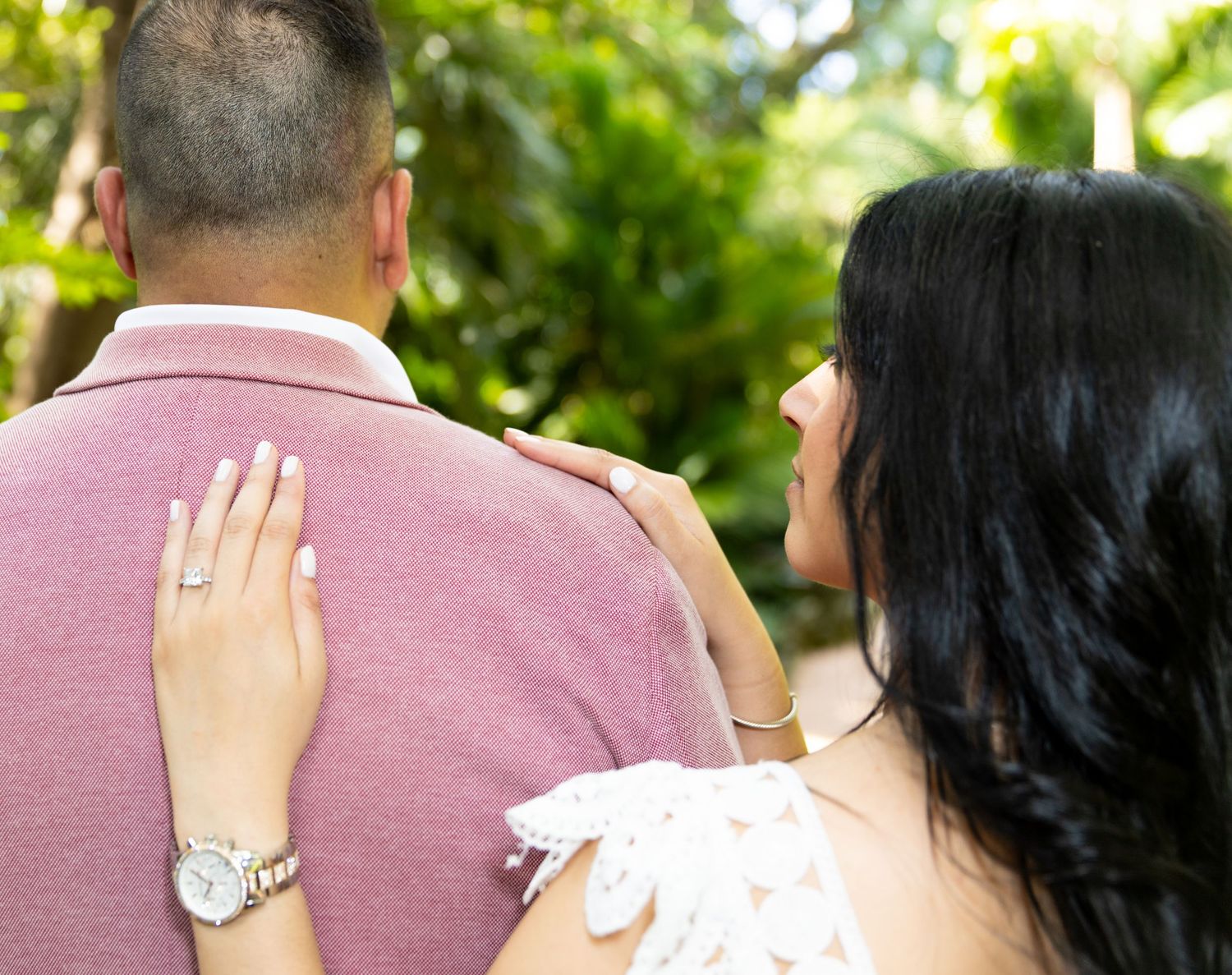 A couple embraces romantically in a garden setting with green foliage in the background.