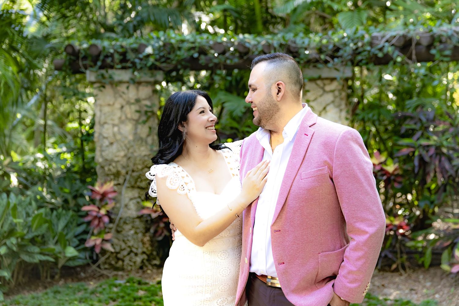 A couple in wedding attire embraces while standing in a lush garden setting during their celebration.