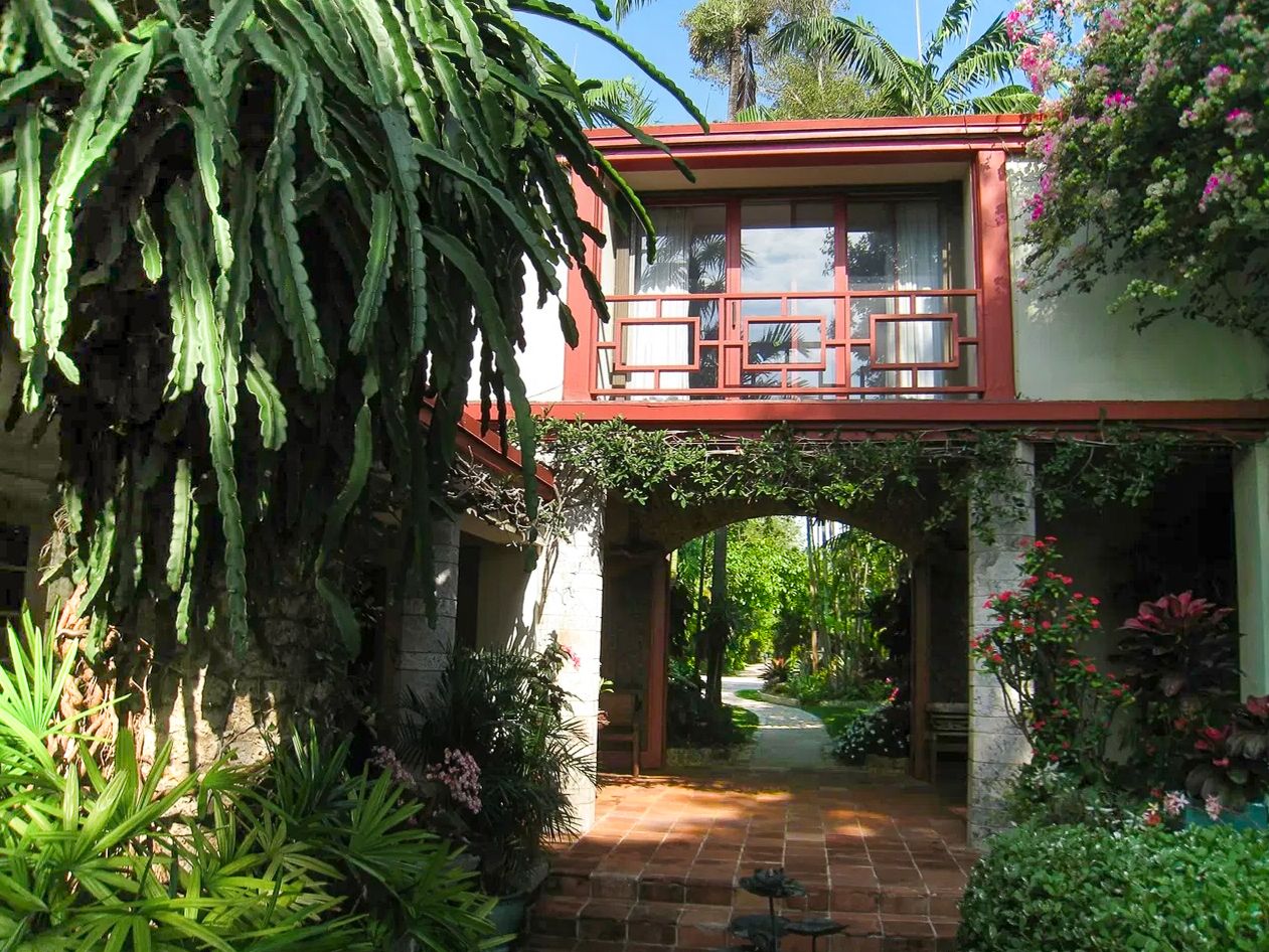 Charming red elevated bridge house connected by a garden path with lush tropical foliage and flowers.
