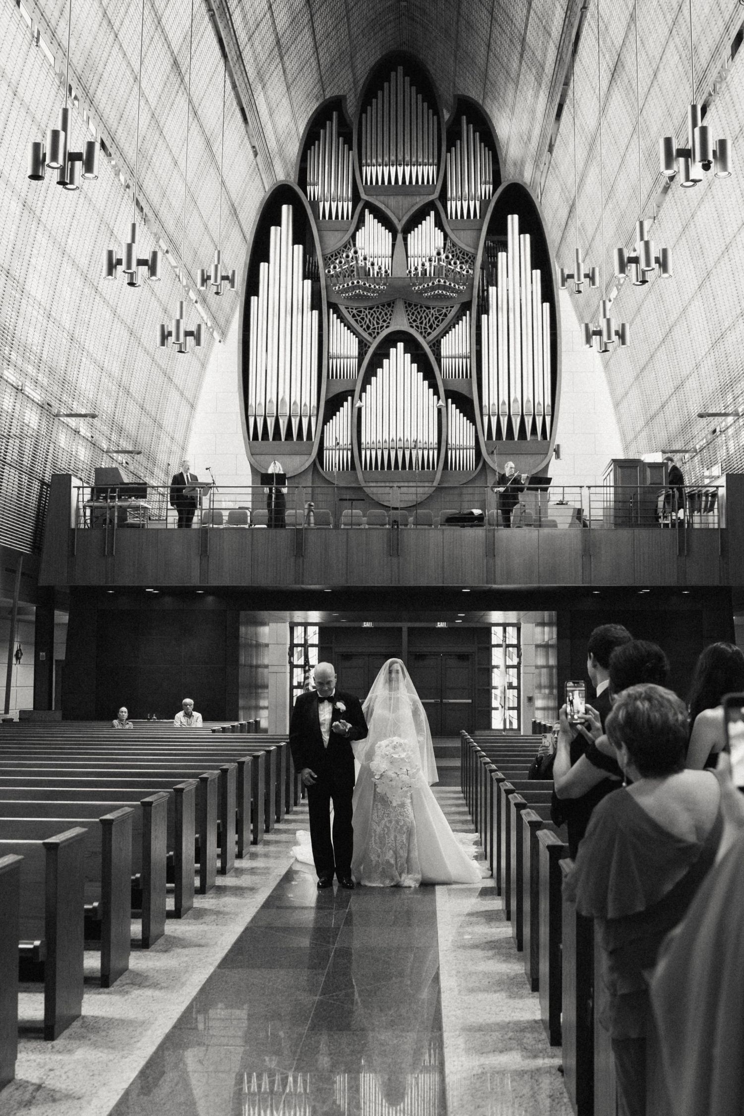 Black and white panoramic view of a church interior during a wedding ceremony with organ pipes visible in the background.
