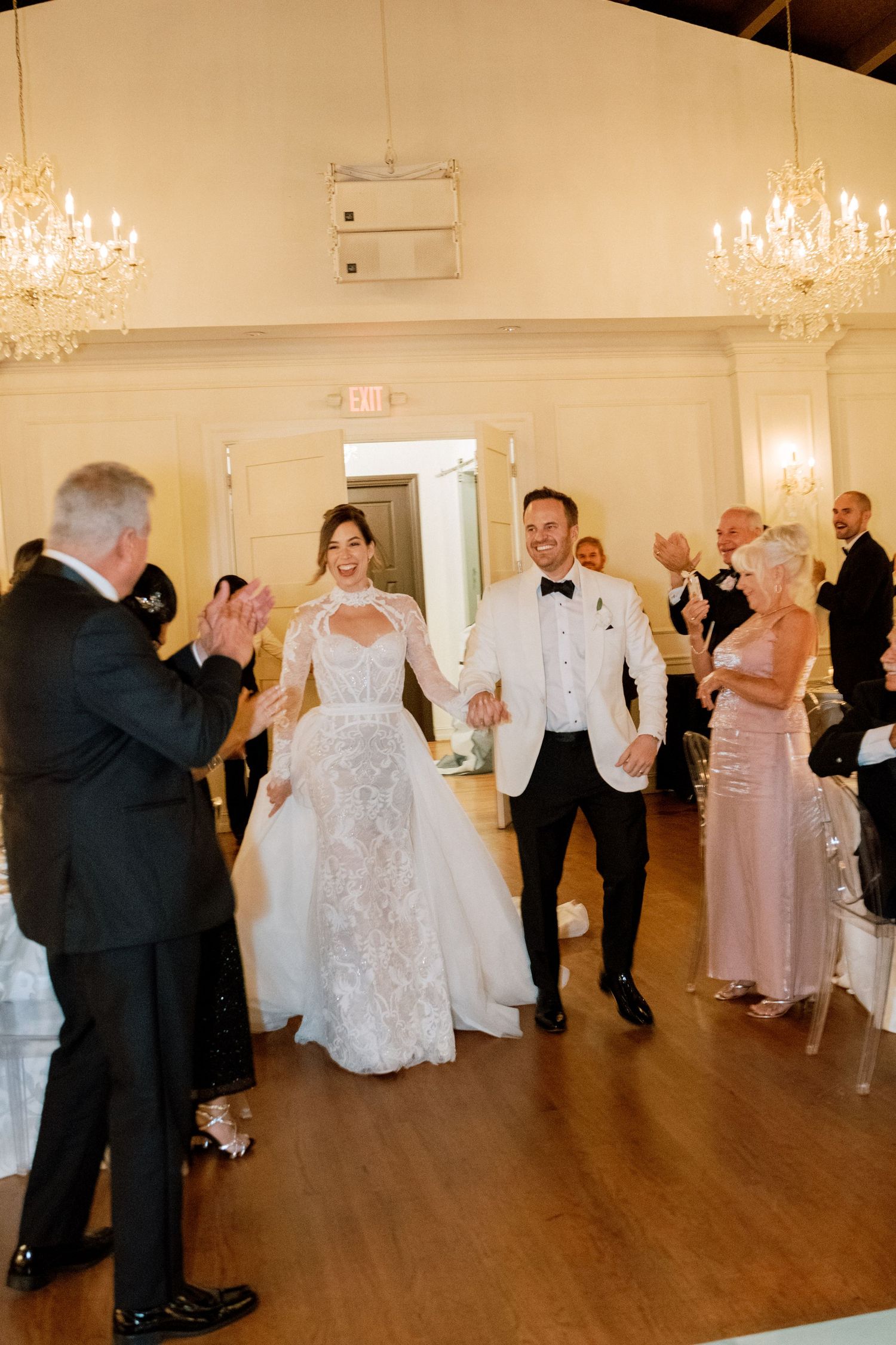 Wedding guests dancing in an elegant ballroom decorated with crystal chandeliers and hardwood floors.