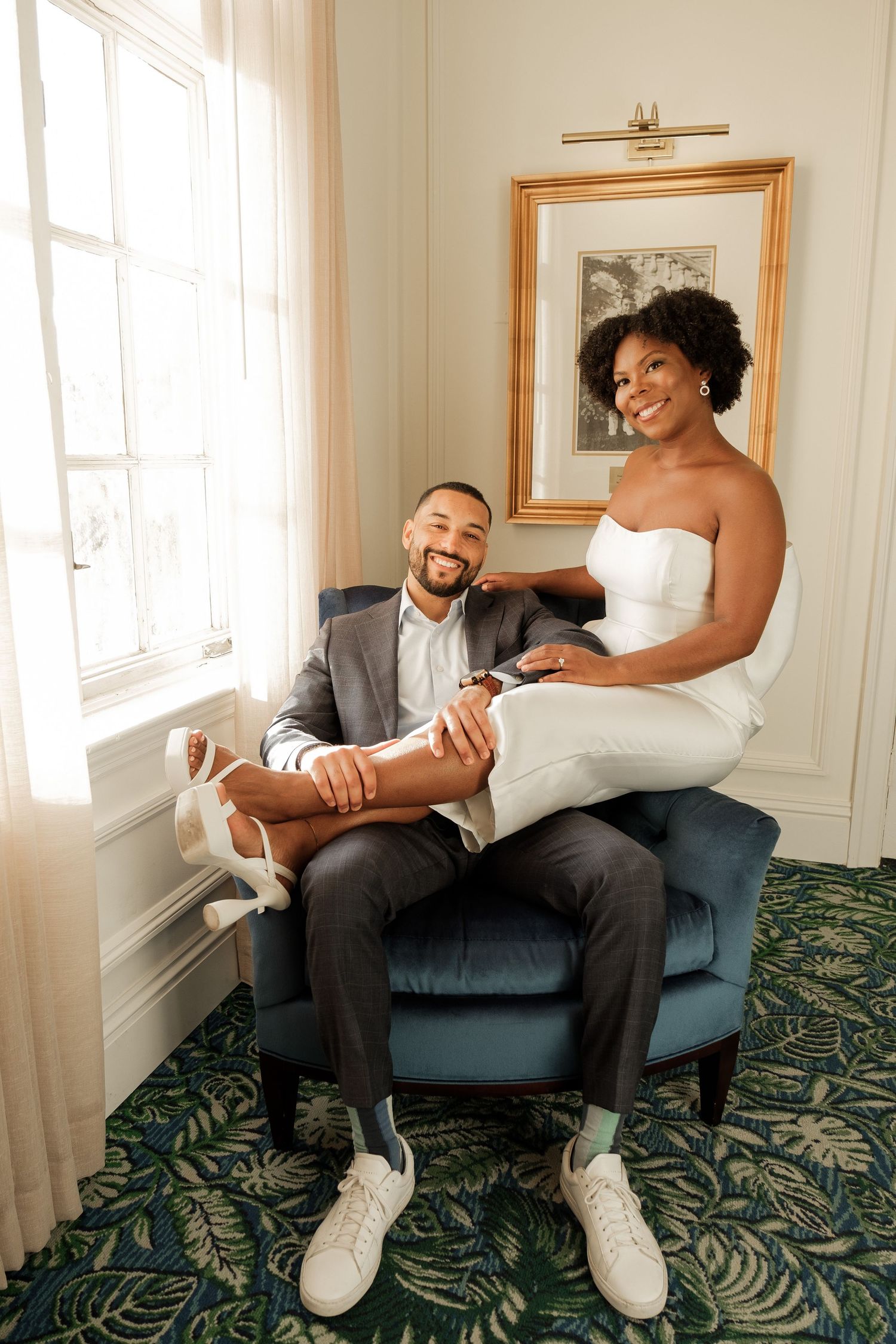 Happy couple shares an intimate moment in elegant room with ornate carpet and window light, dressed in wedding attire.