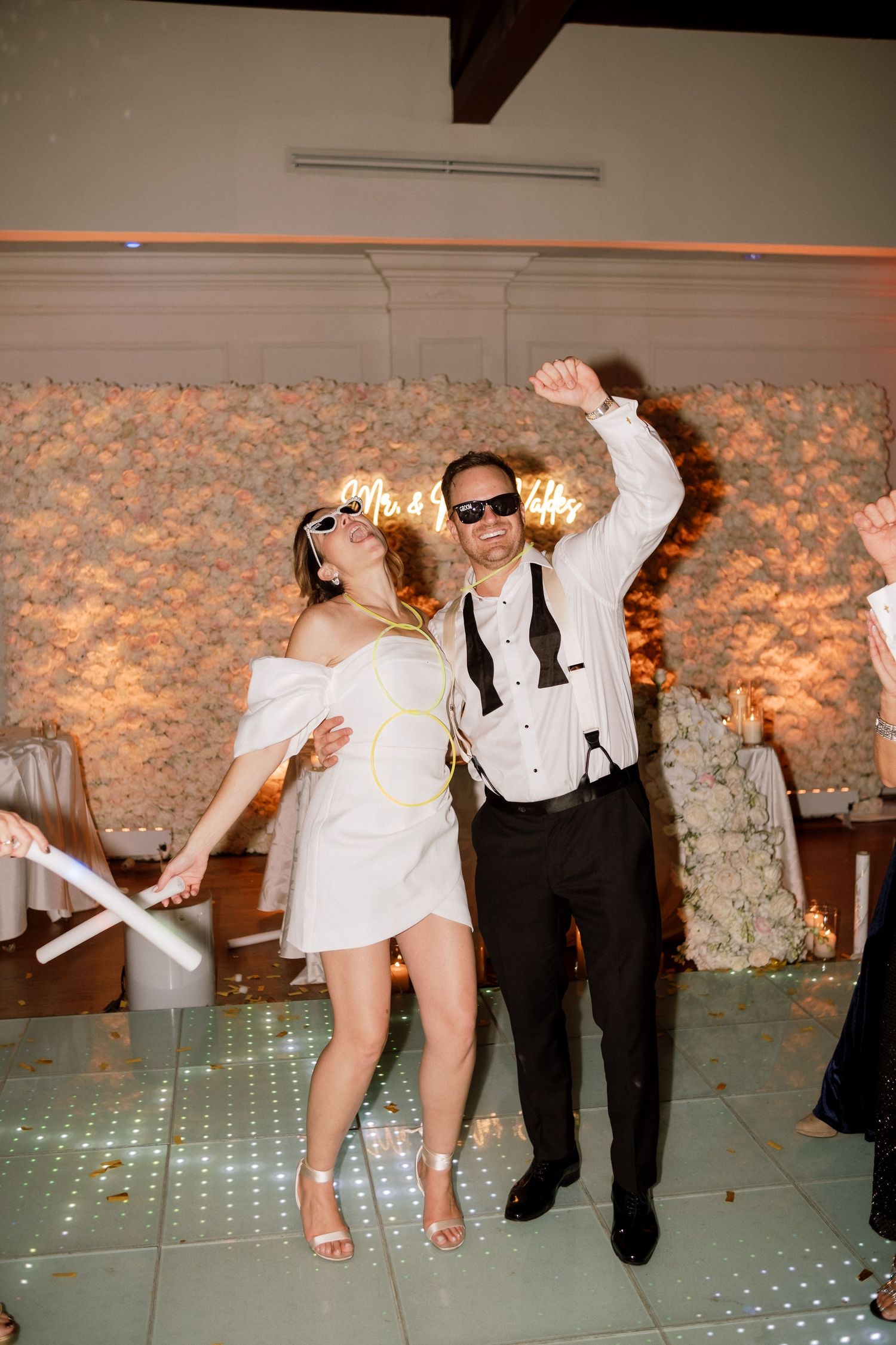 Wedding party members perform energetic dance moves on an illuminated dance floor.