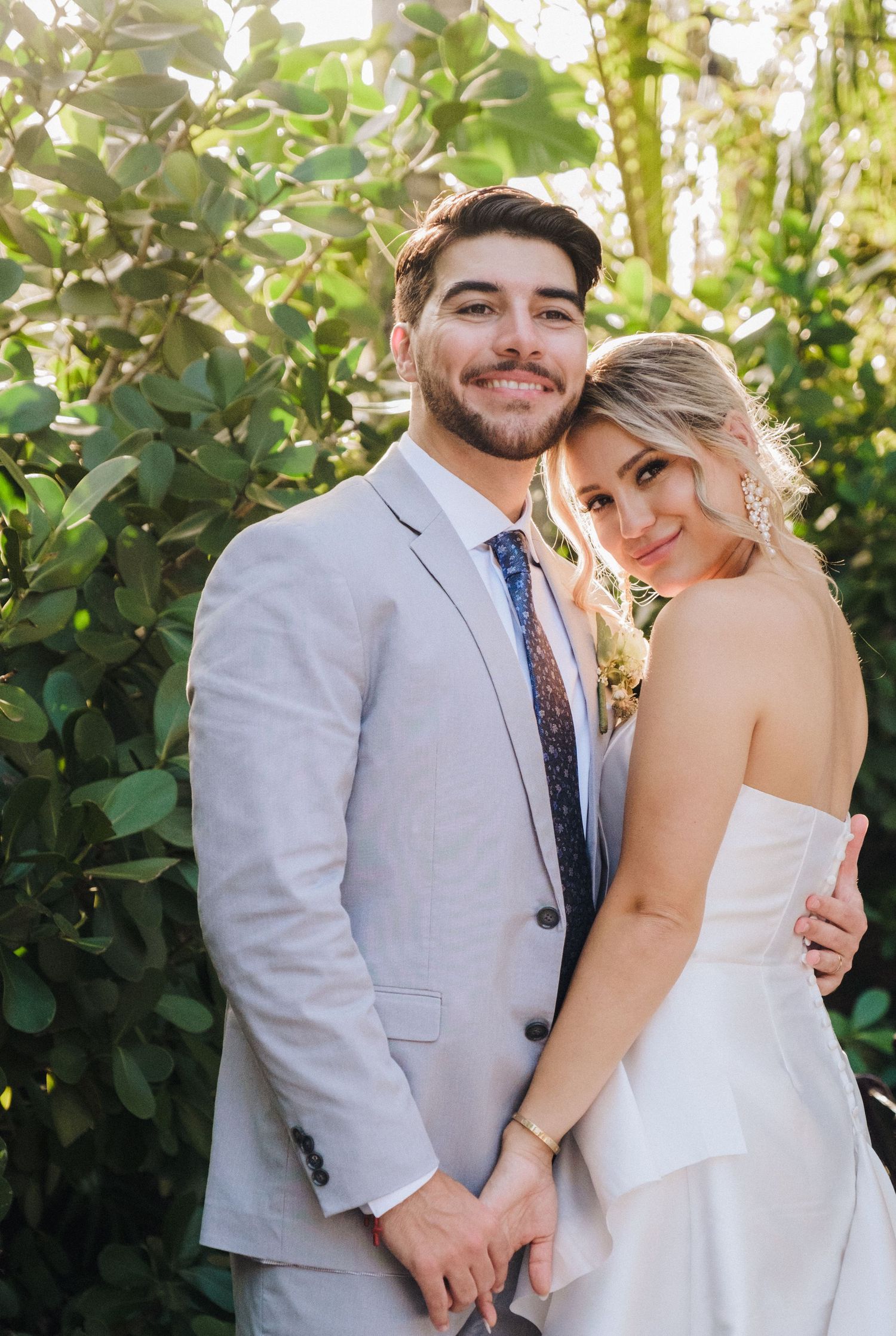 A wedding couple shares intimate moments against a lush green garden backdrop in summer.