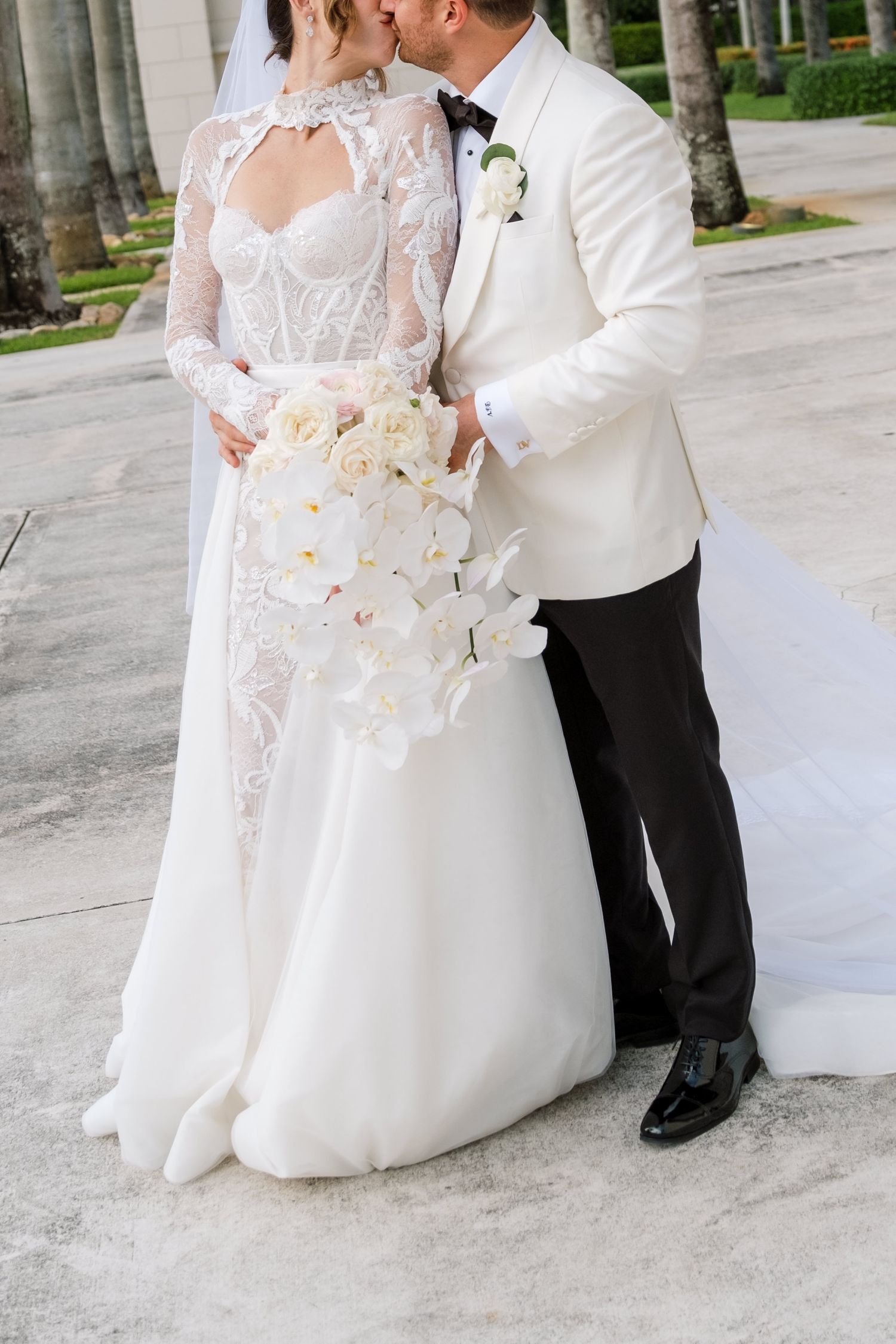 Wedding couple shares an intimate moment with white orchid bouquet in an outdoor setting.