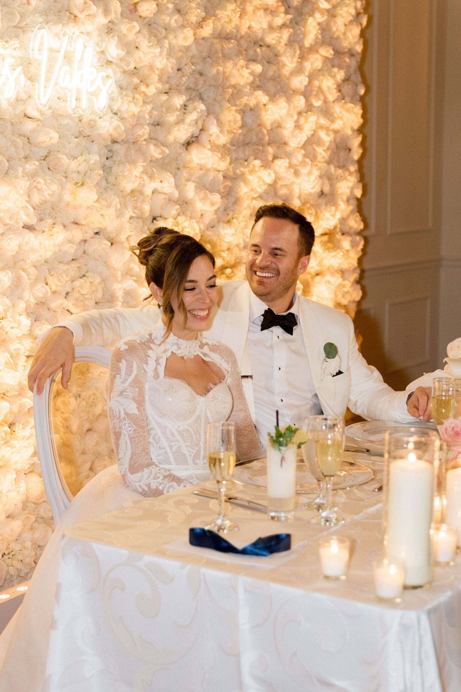 Wedding party sits at head table with glowing backdrop and candles.