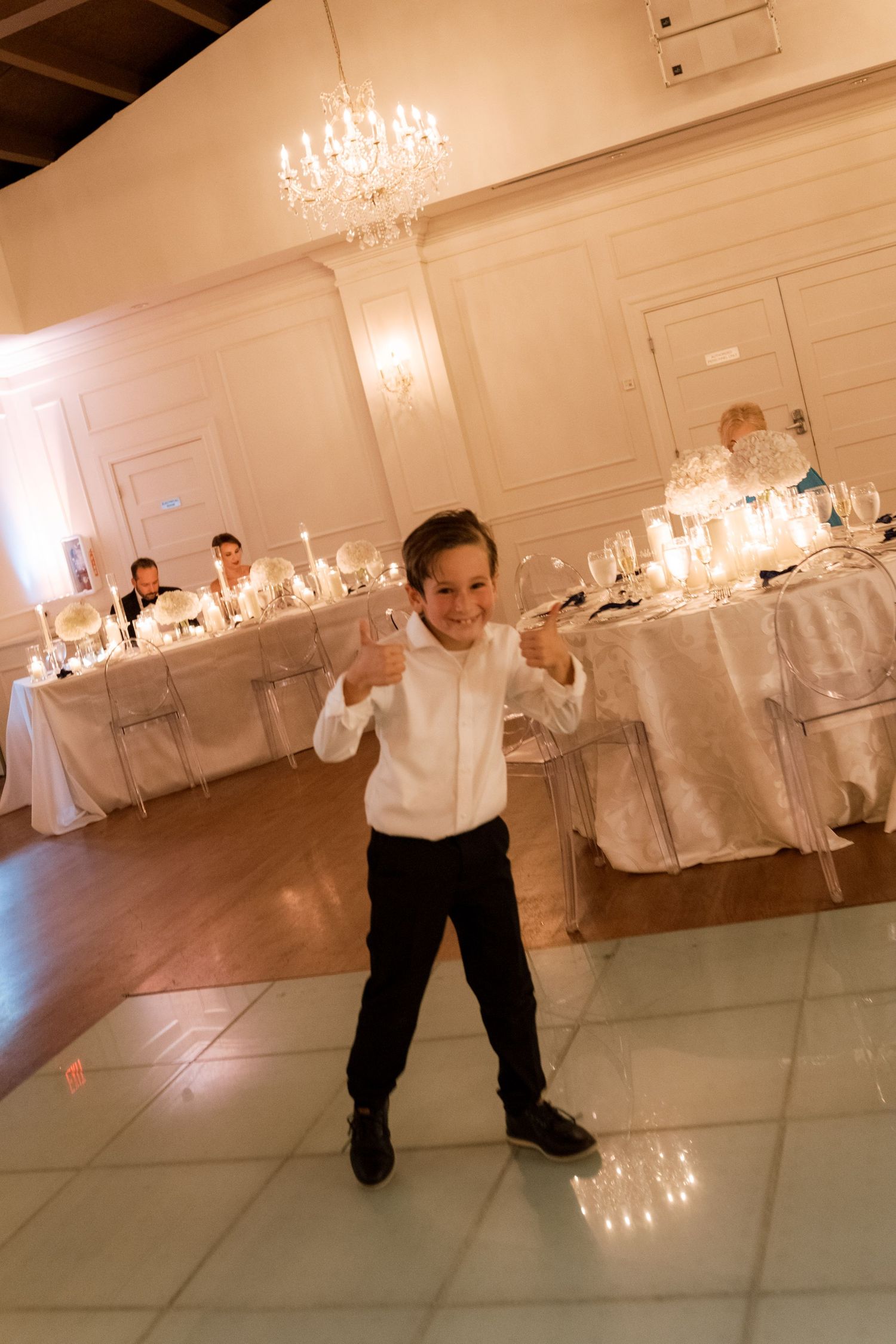 Elegant white reception hall with crystal chandeliers and formal table settings.