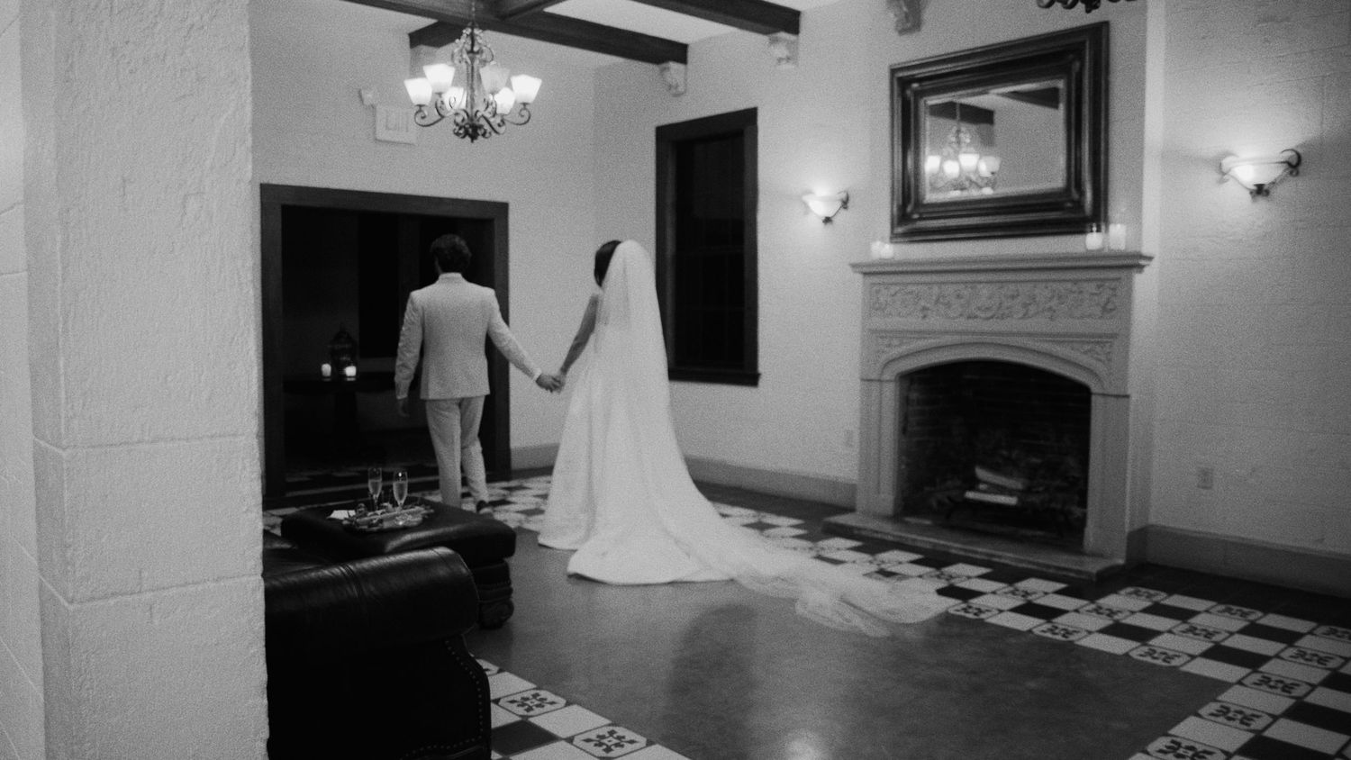 Black and white panoramic view of an elegant wedding venue interior with checkered floors and ornate wall sconces.