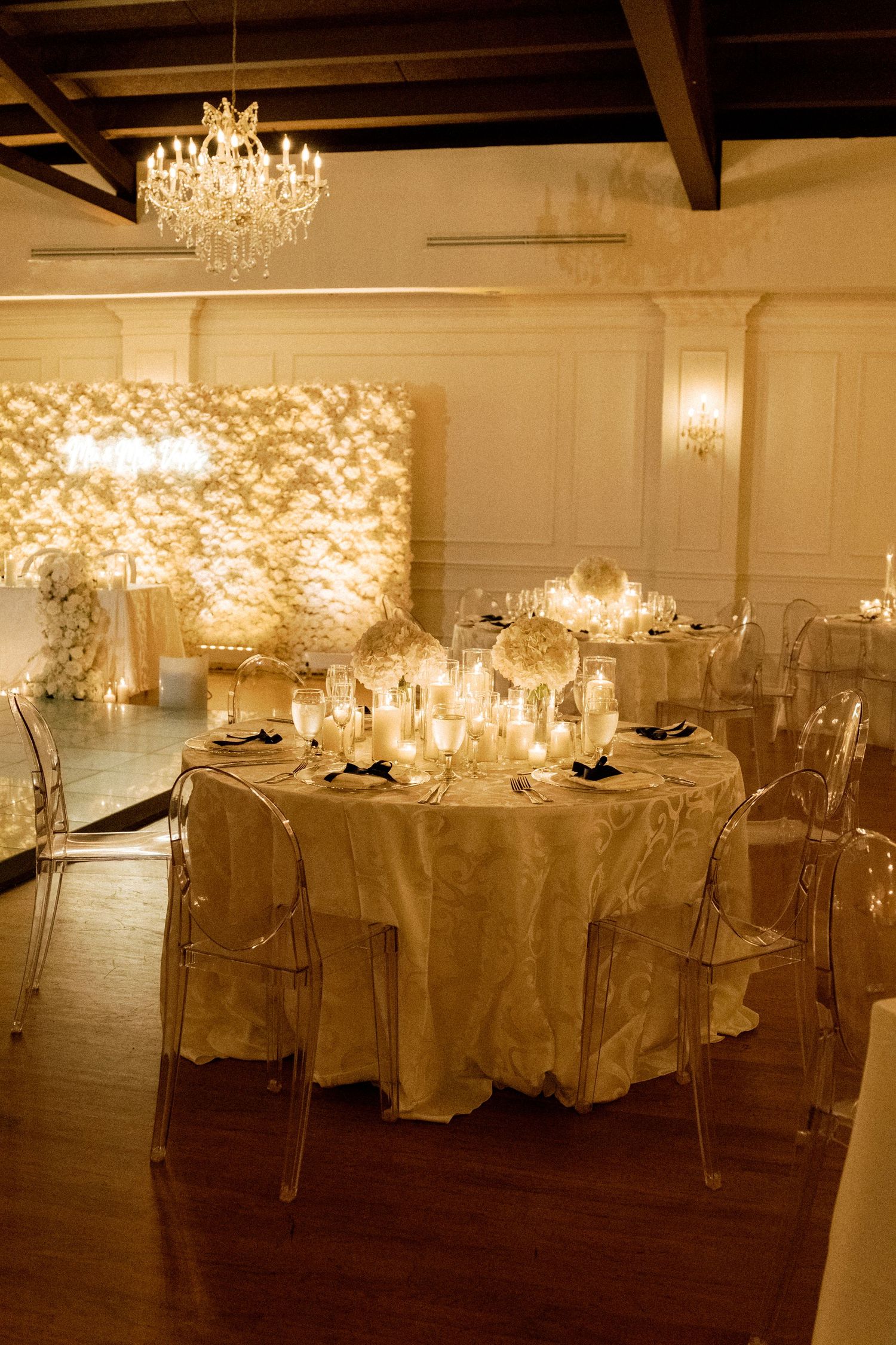 An elegant wedding reception venue with crystal chandeliers and white-covered tables arranged in rows.