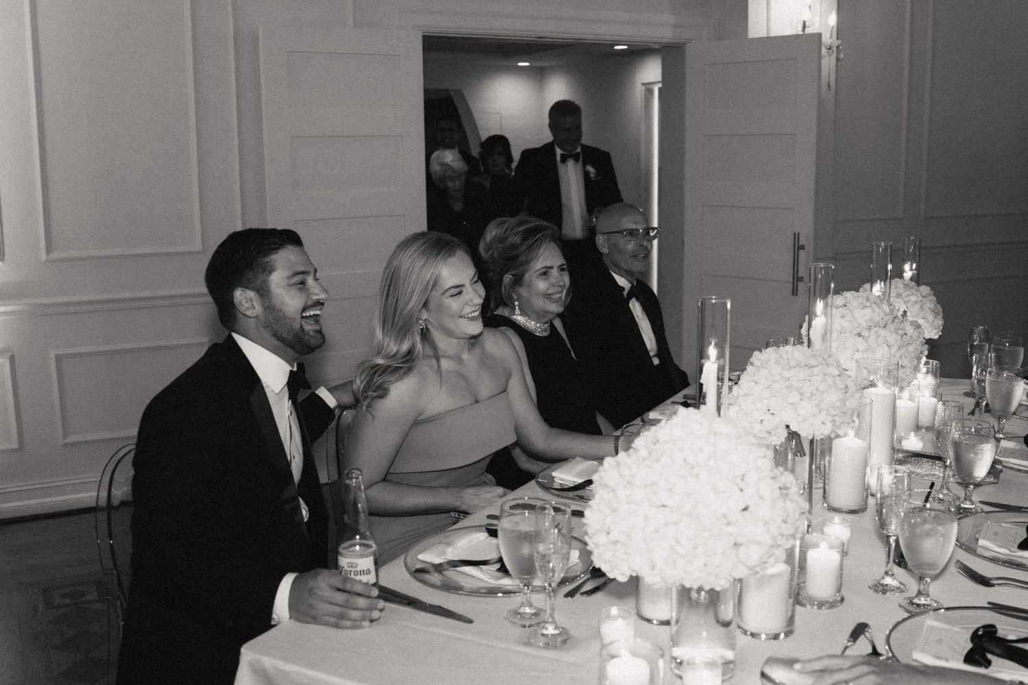 Wedding reception guests enjoy dinner at elegantly set tables with white linens and centerpieces.