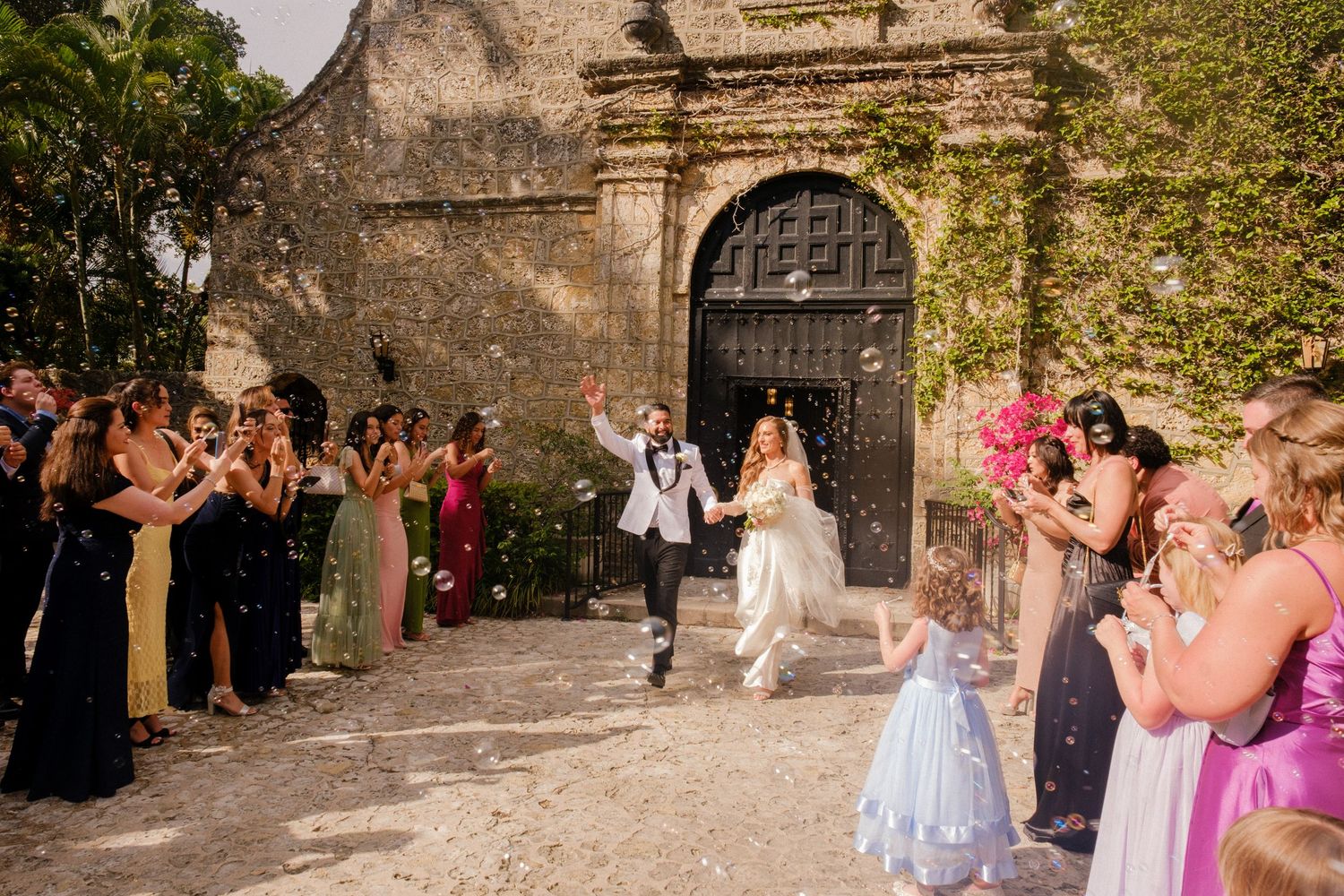 Wedding guests gathered in a stone courtyard tossing flower petals during an outdoor celebration.