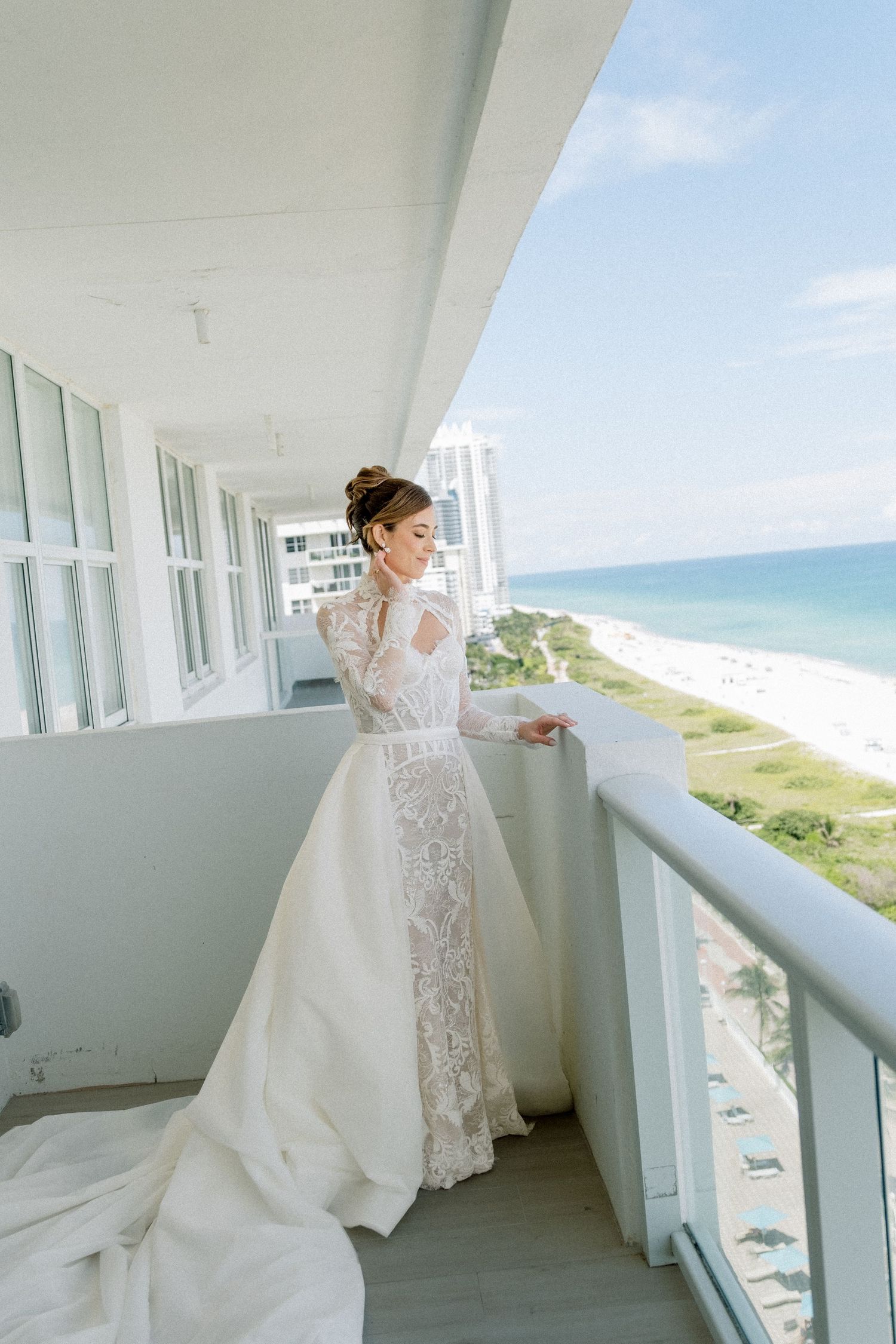 A bride in a flowing white lace gown twirls gracefully on an oceanfront balcony with coastal views.