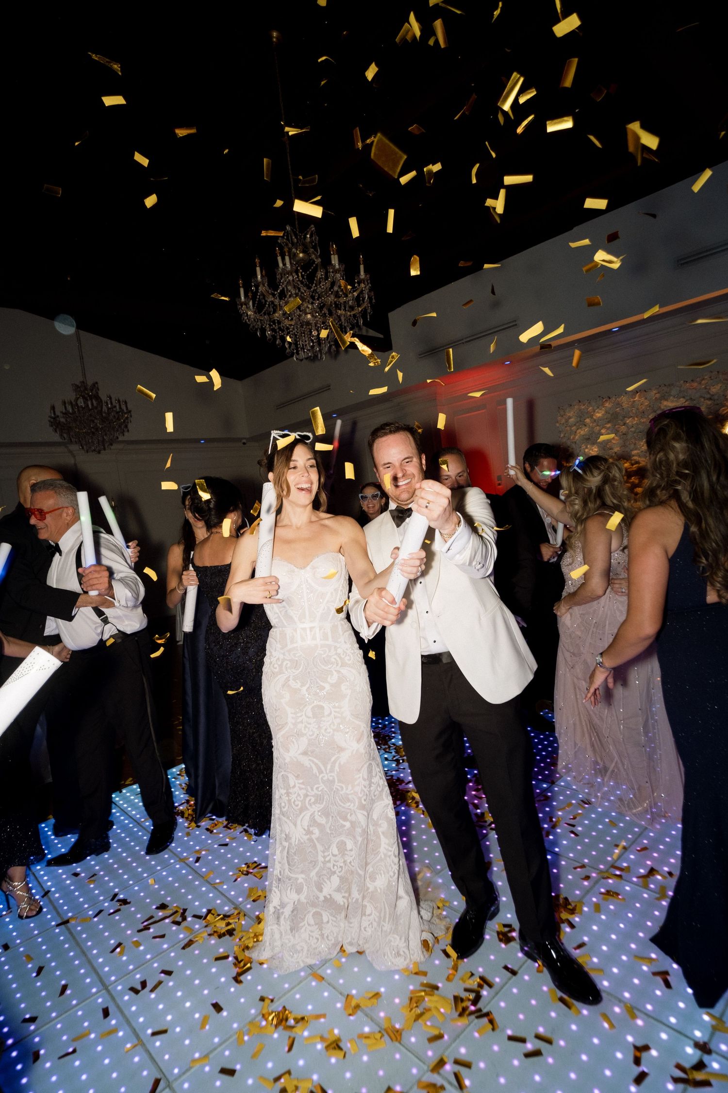 Wedding celebration with gold confetti falling on dance floor under dramatic lighting.