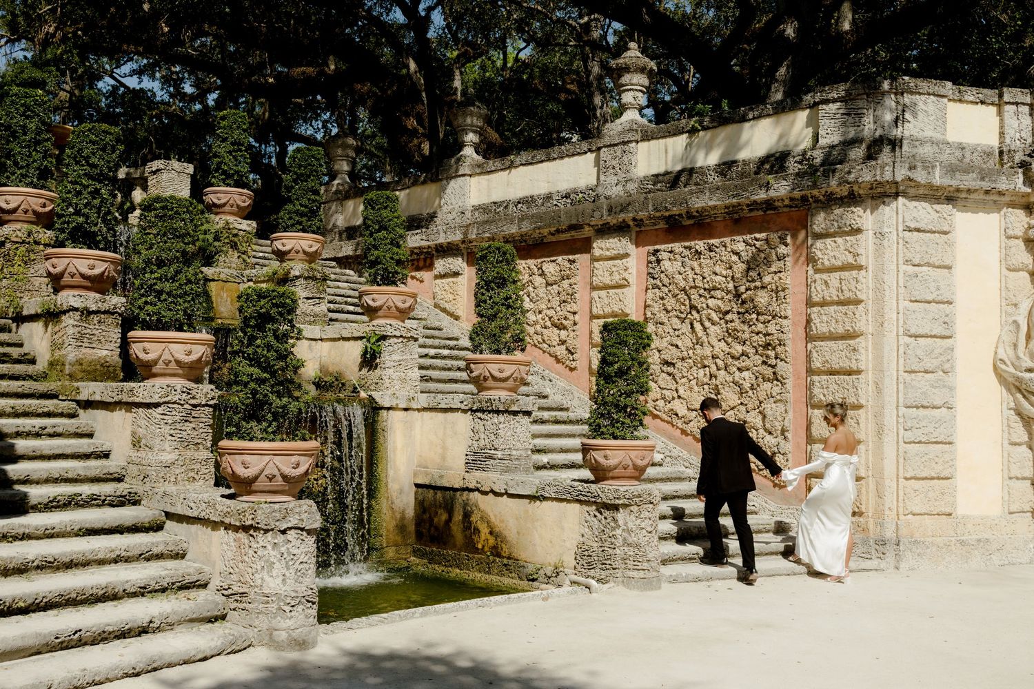 Ancient stone staircase with ornate railing and weathered walls leading up through a terraced Mediterranean garden.