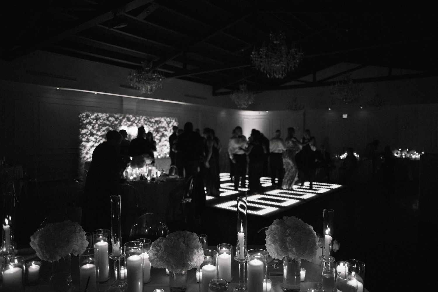 Dark nighttime reception venue with ambient lighting and silhouettes of guests dancing.