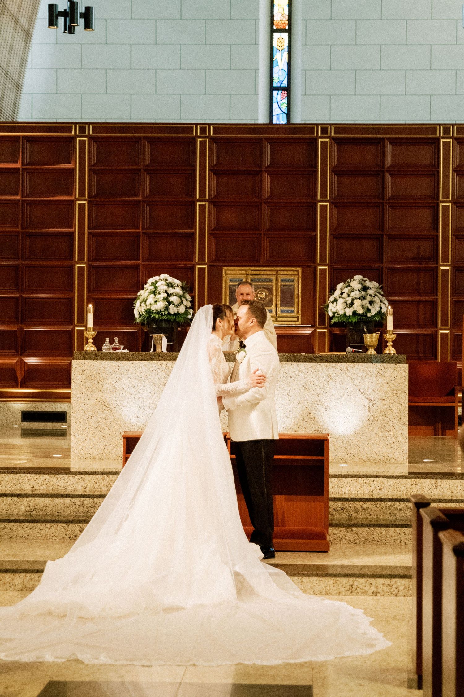 A romantic wedding ceremony scene in a church with wooden pews and white floral decorations.