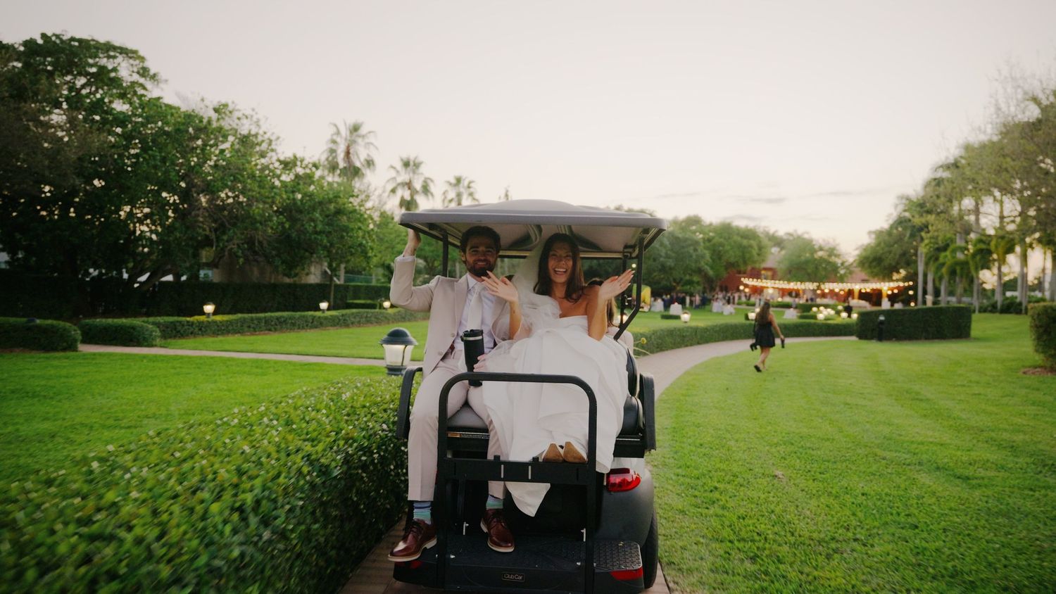 People riding together in a white golf cart along a scenic green lawn path on a sunny day at a golf course.