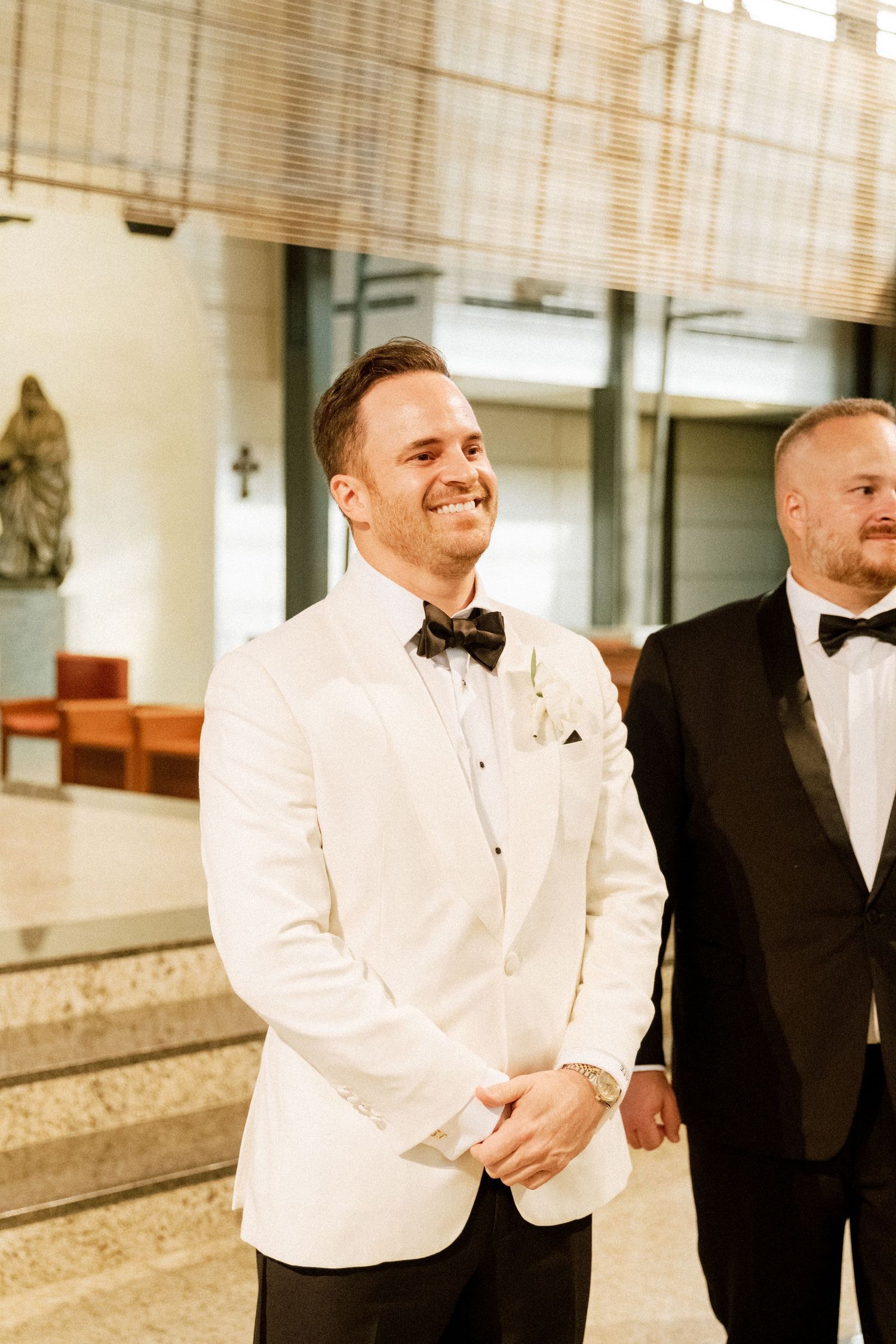 Two men in formal attire share a candid moment, one wearing a white dinner jacket and the other in black.