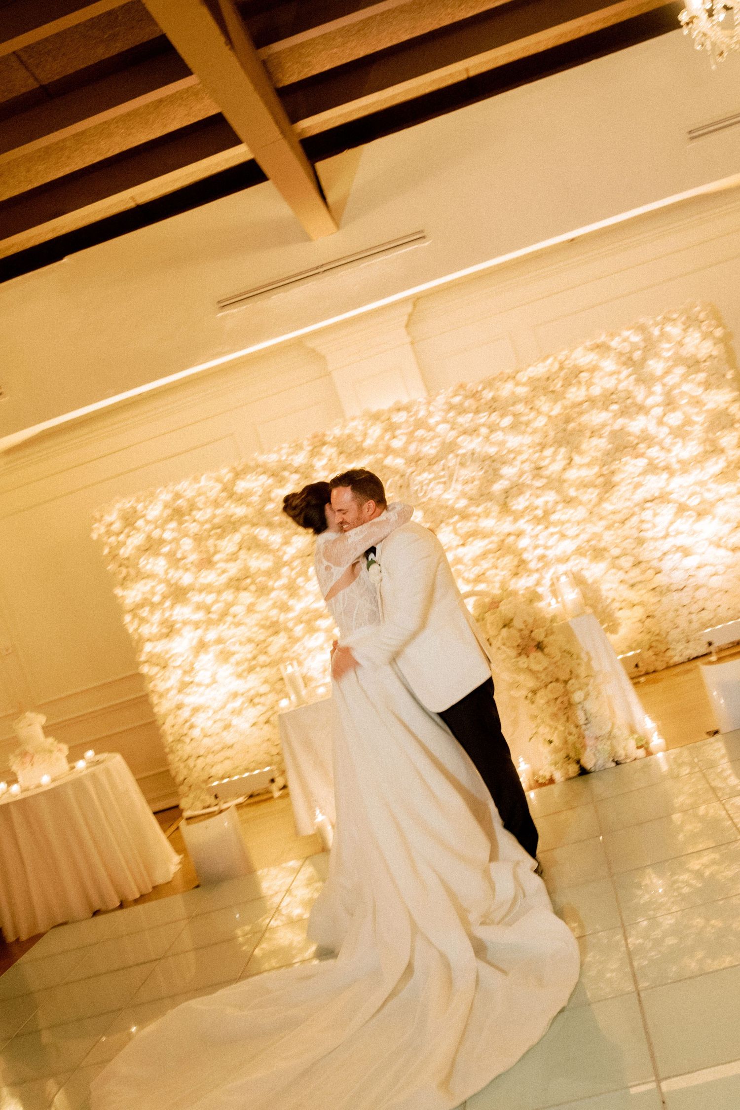 Romantic first dance in a ballroom with illuminated backdrop and wooden beam ceiling.