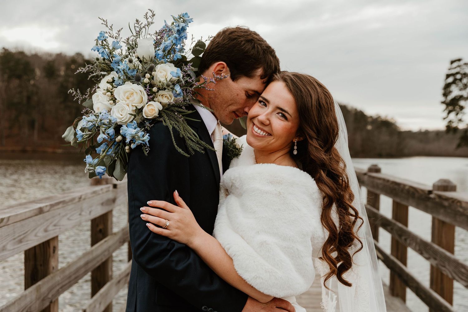 A romantic wedding couple embraces on a rustic wooden bridge surrounded by natural scenery.