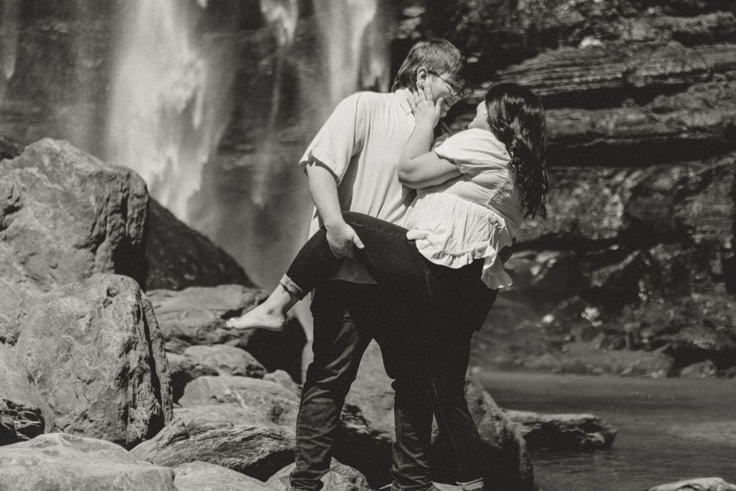 Vintage black and white photo of a romantic couple embracing by a scenic waterfall.