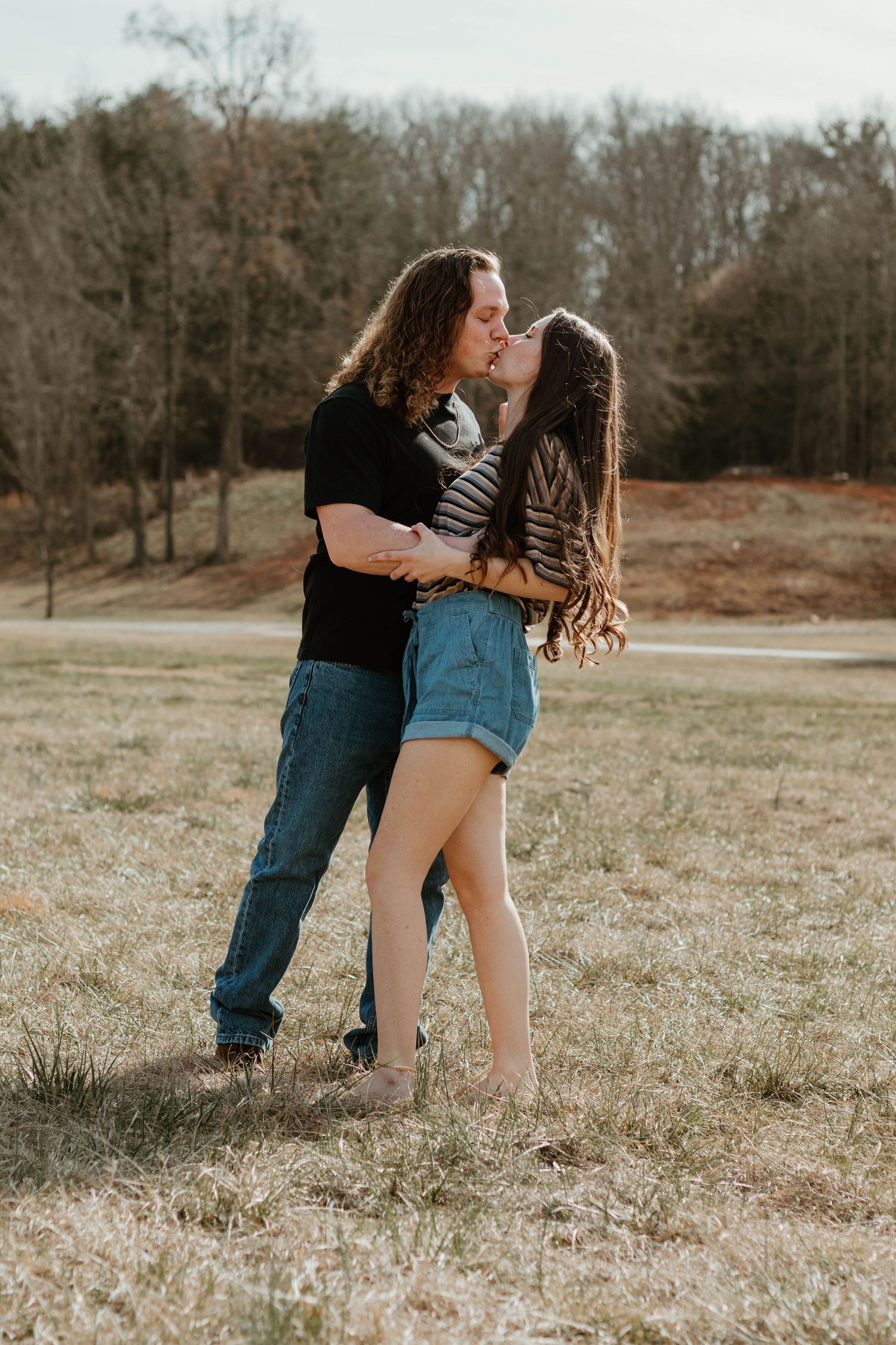 Couple sharing romantic embrace in field with trees in background in north Georgia.