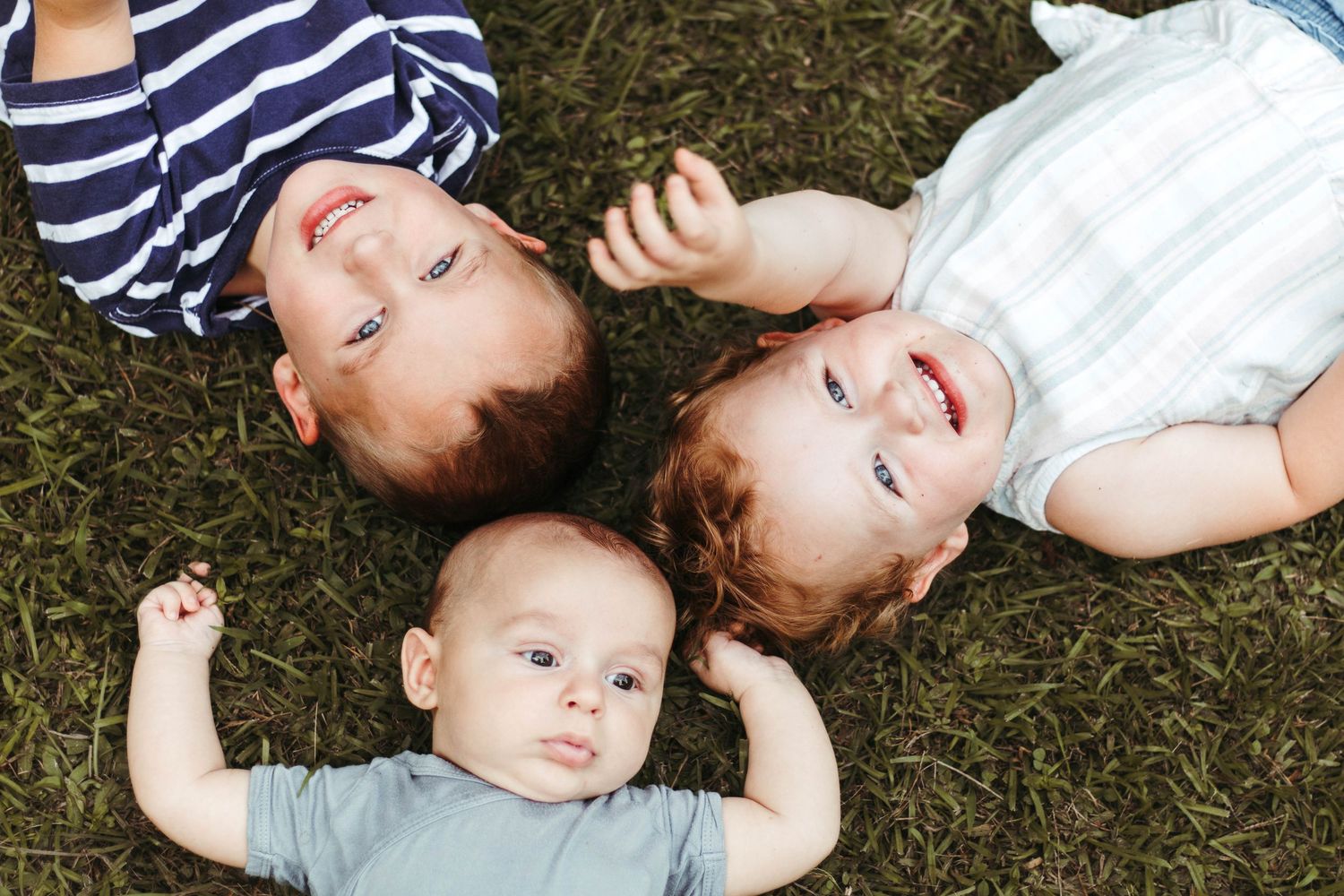 Three young children lying on grass looking upward on a sunny day at Henderson Falls Park in Toccoa, Georgia.