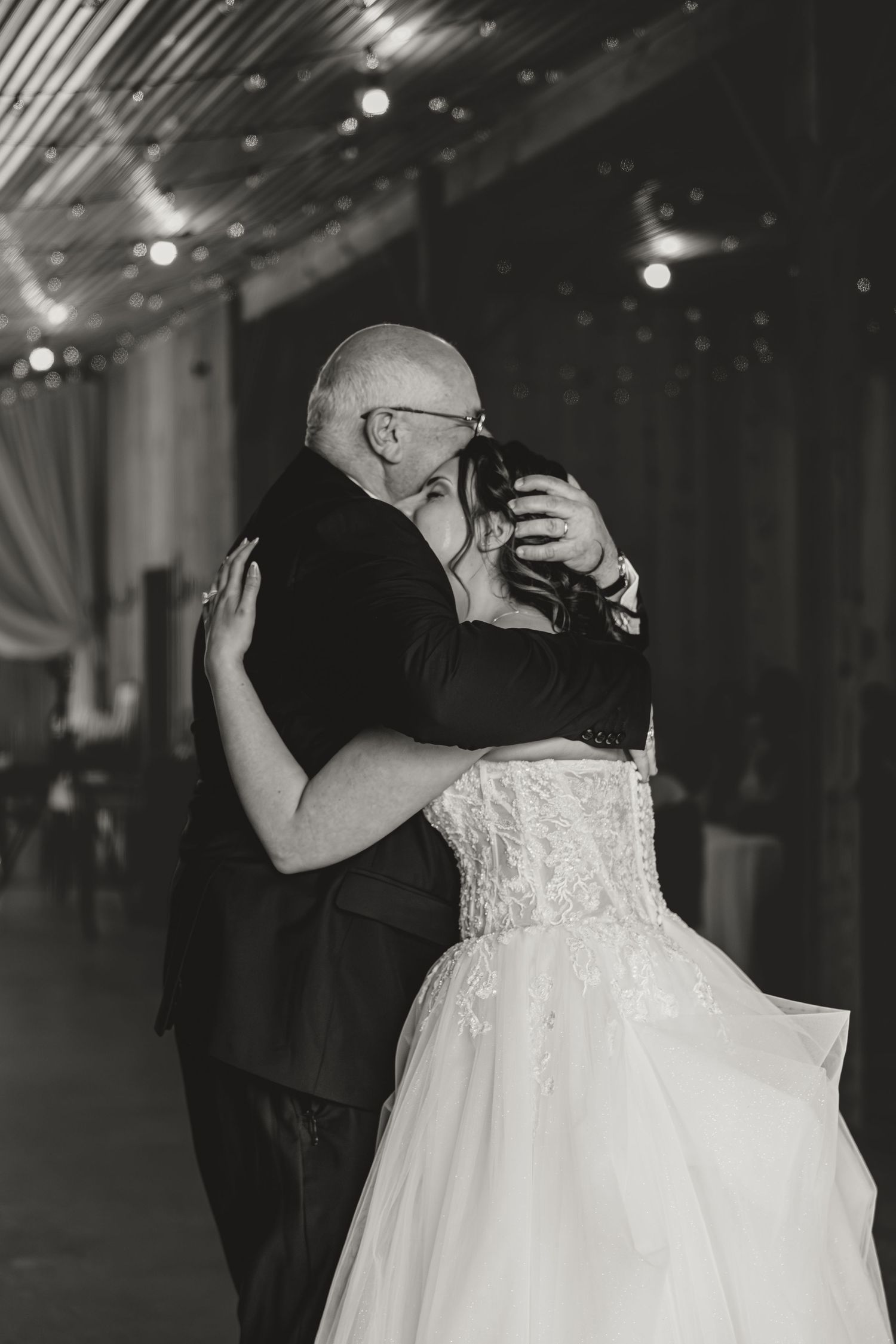Emotional black and white photo of bride and bald groom sharing tender embrace on wedding dance floor.