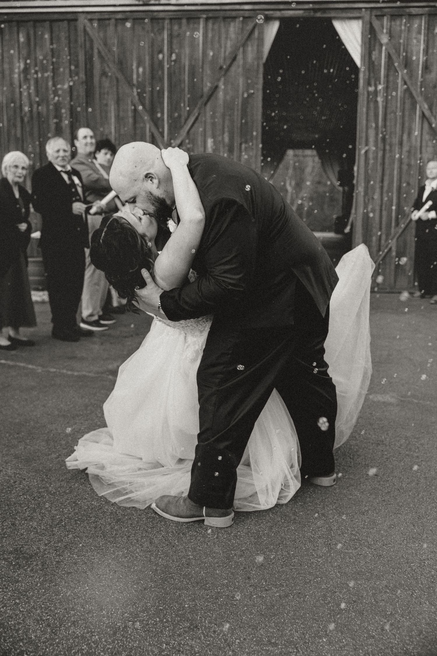 Groom dips bride for romantic kiss during first dance at rustic barn wedding reception.