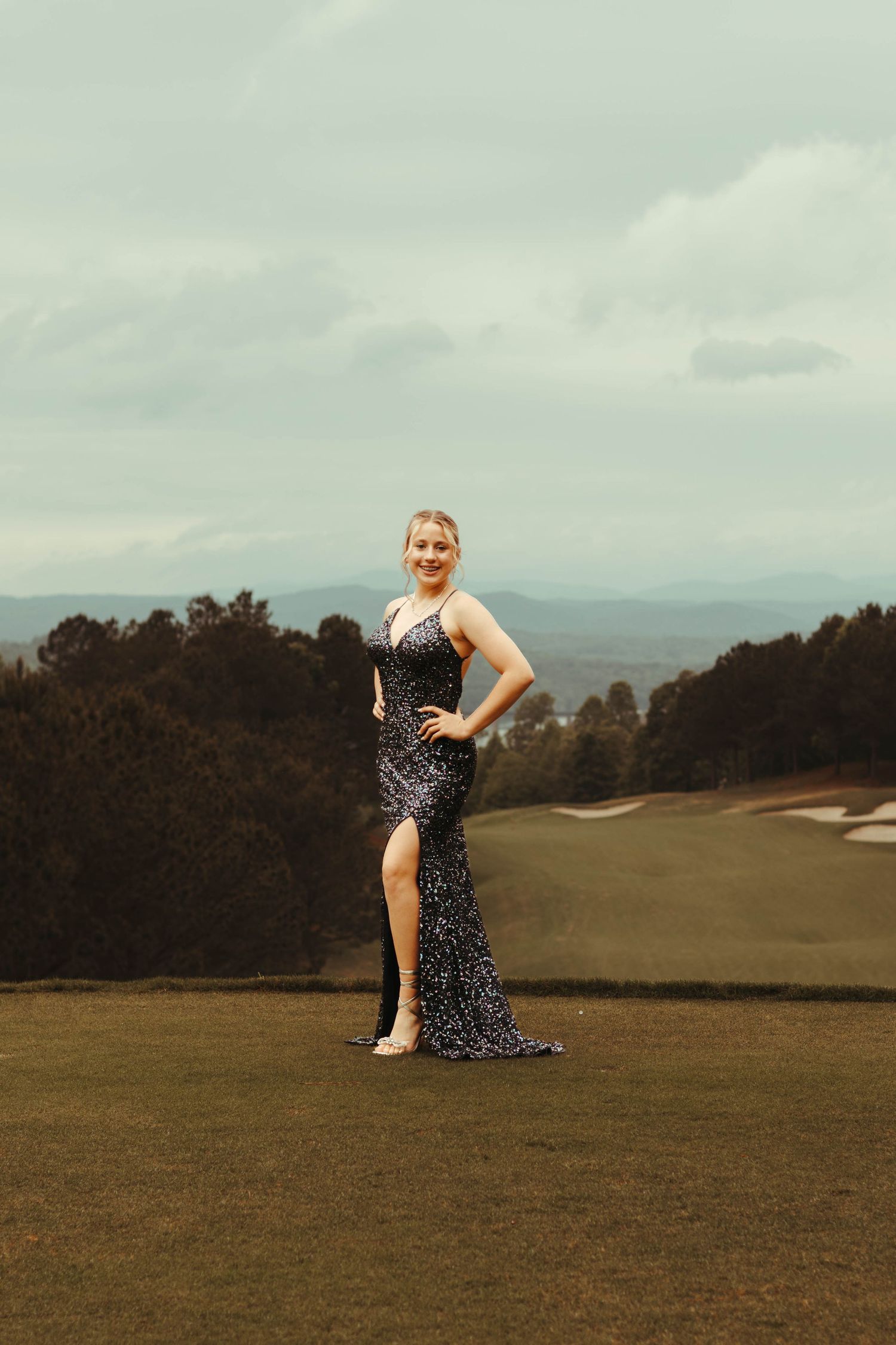 Someone in a sparkly formal evening gown poses on a scenic golf course with mountains in the background at sunset at the Currahee Club.