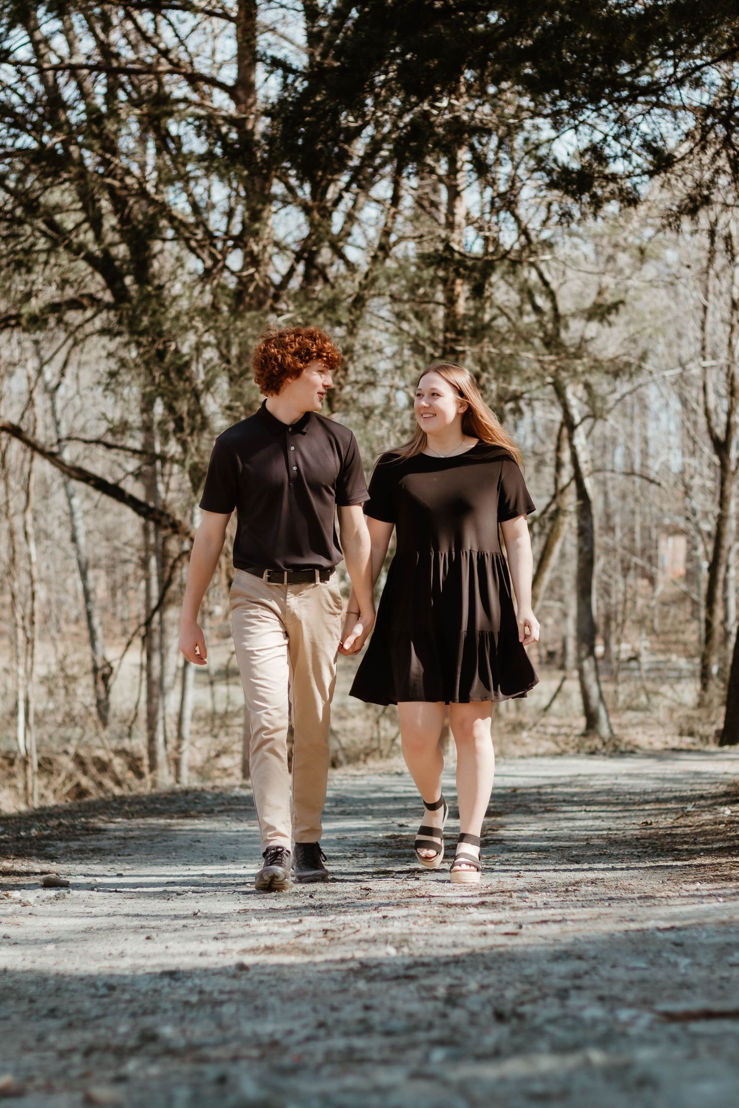 A couple walks hand in hand on a wooded path wearing coordinating black outfits on a sunny day in northeast Georgia.
