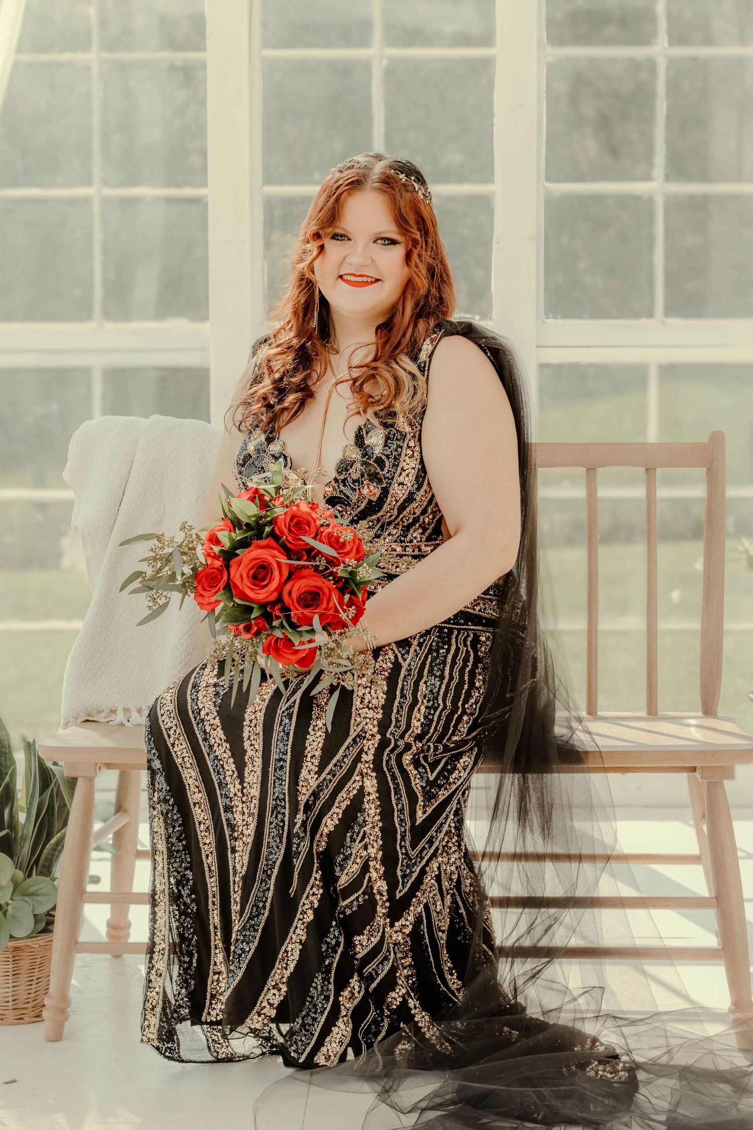 Person in sparkly formal dress holds vibrant red rose bouquet in sunlit greenhouse setting at The Farm at Daffodil Hil.