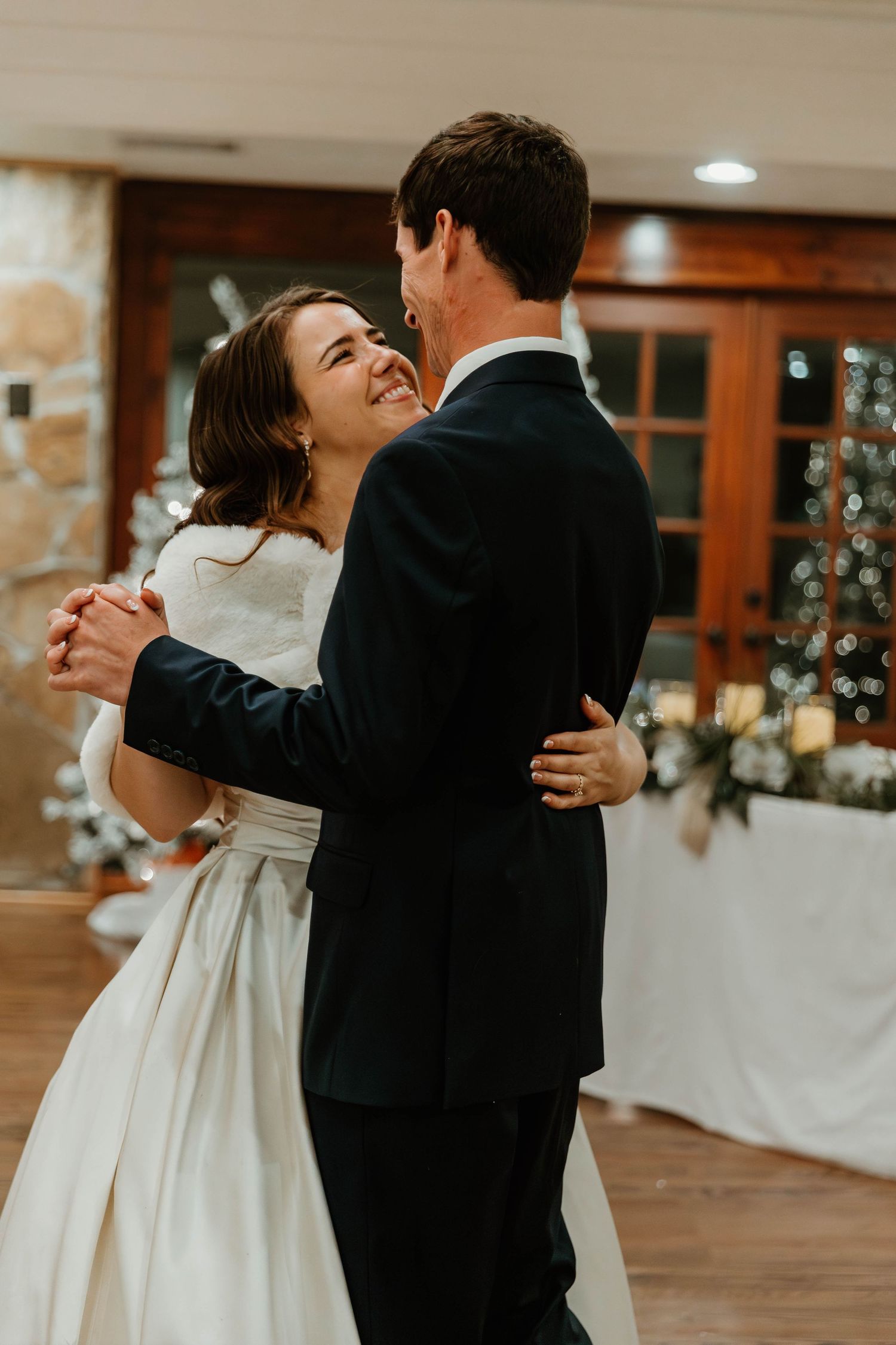 Bride and groom share an intimate dance moment on a wooden floor with holiday decor visible in the background.