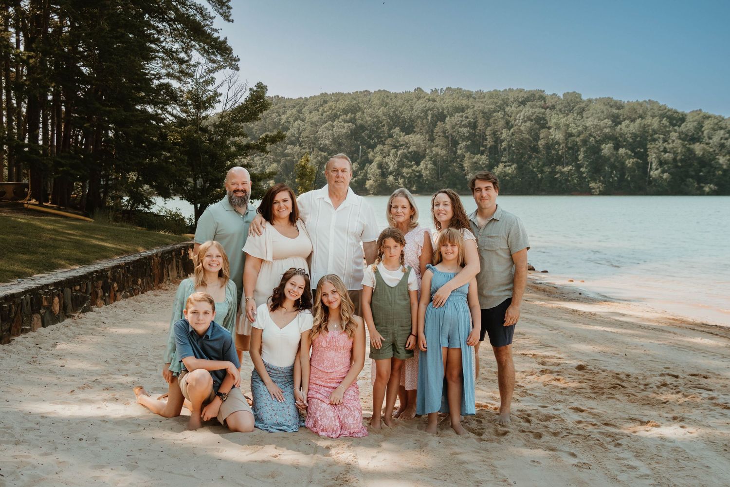 Family group sitting on sandy beach at Tugaloo State Park together wearing coordinated blue and neutral colored outfits at sunset.
