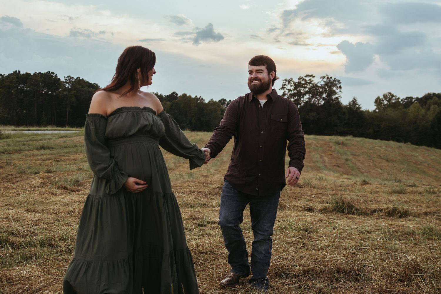 A couple walking hand in hand through a serene field at dusk for a maternity photo session in Northeast Georgia.