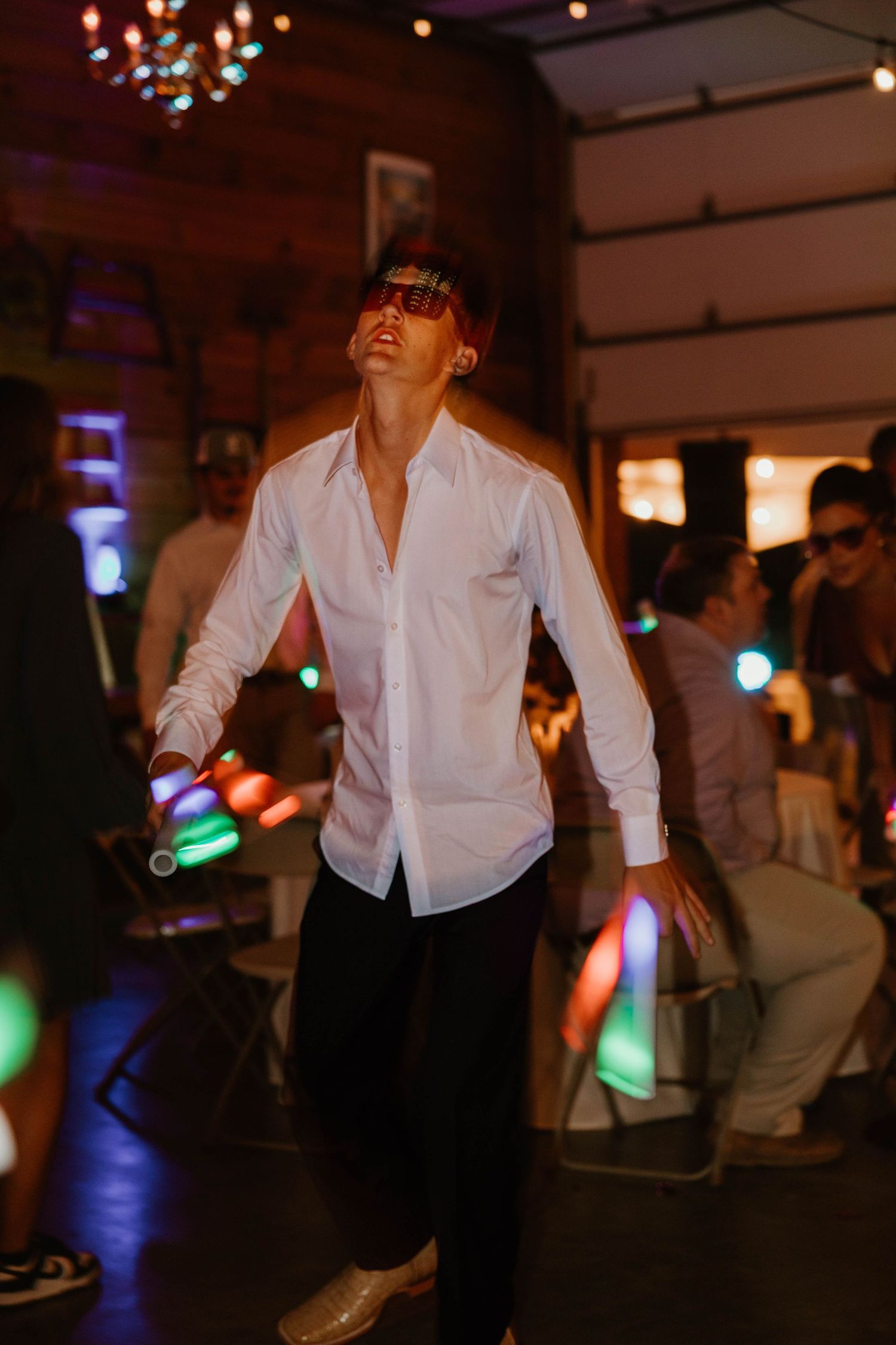 Low-light dance floor scene with party guests dancing under ambient lighting and bokeh effects.