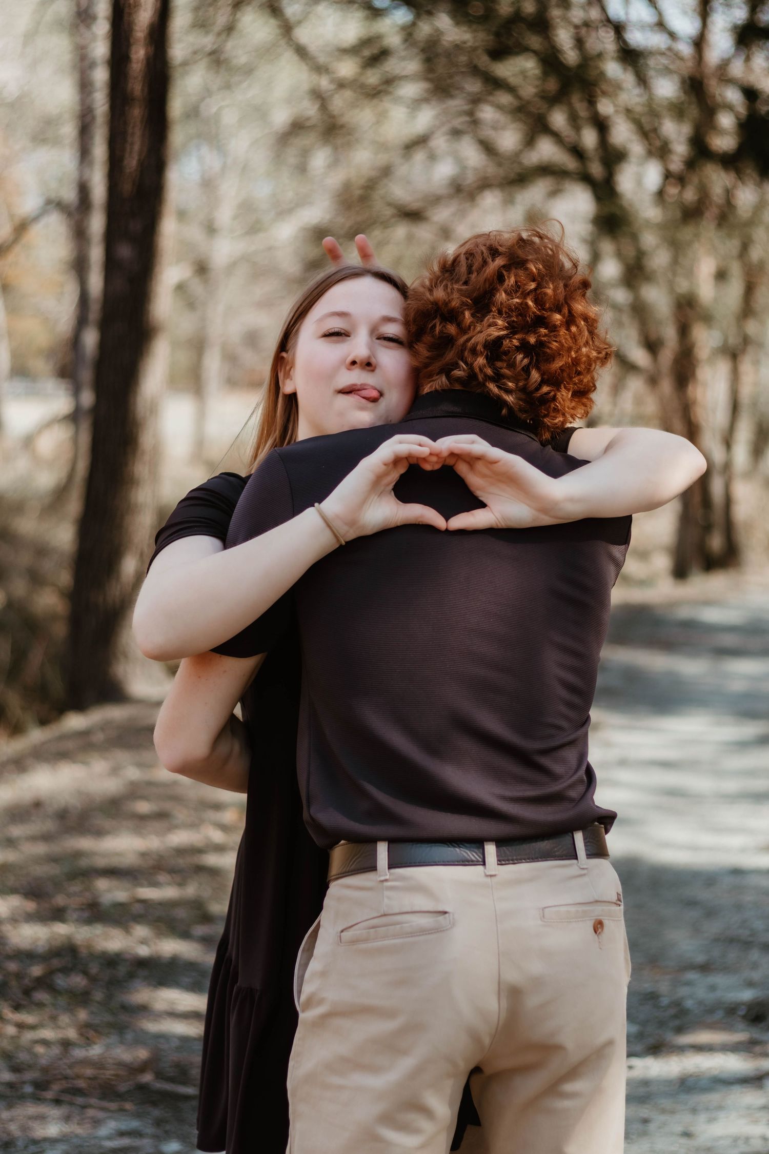 Couple embracing and forming heart shape with hands in wooded setting in north Georgia.