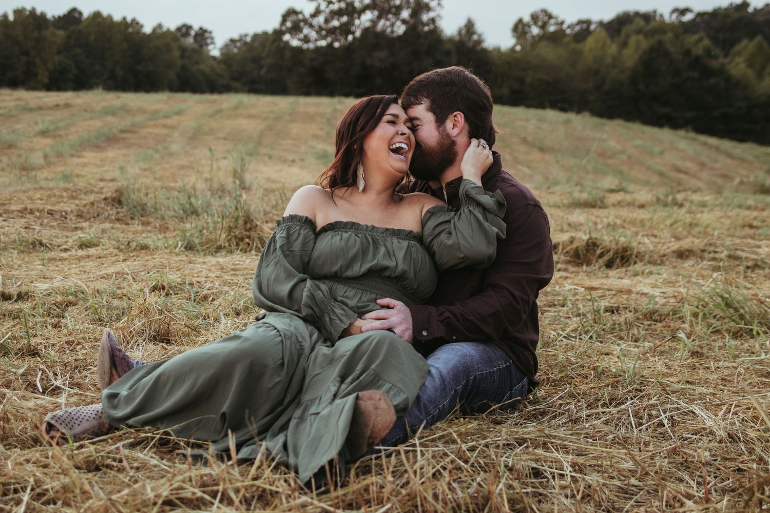A couple sharing an intimate moment while sitting in a golden field at sunset for a maternity photo in Toccoa, GA.