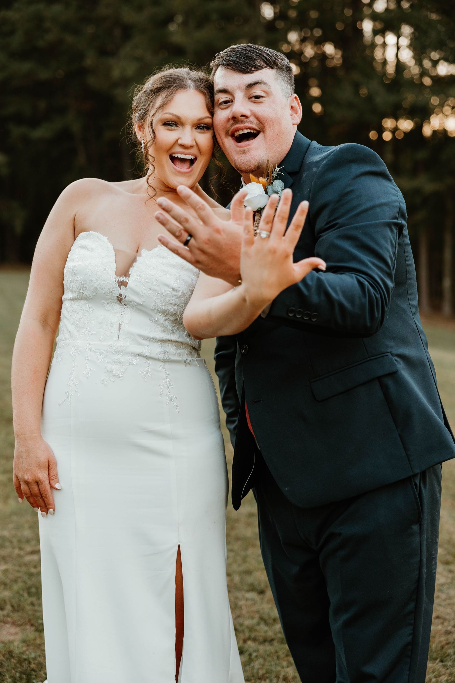 A couple shows off their wedding rings while laughing together at sunset.