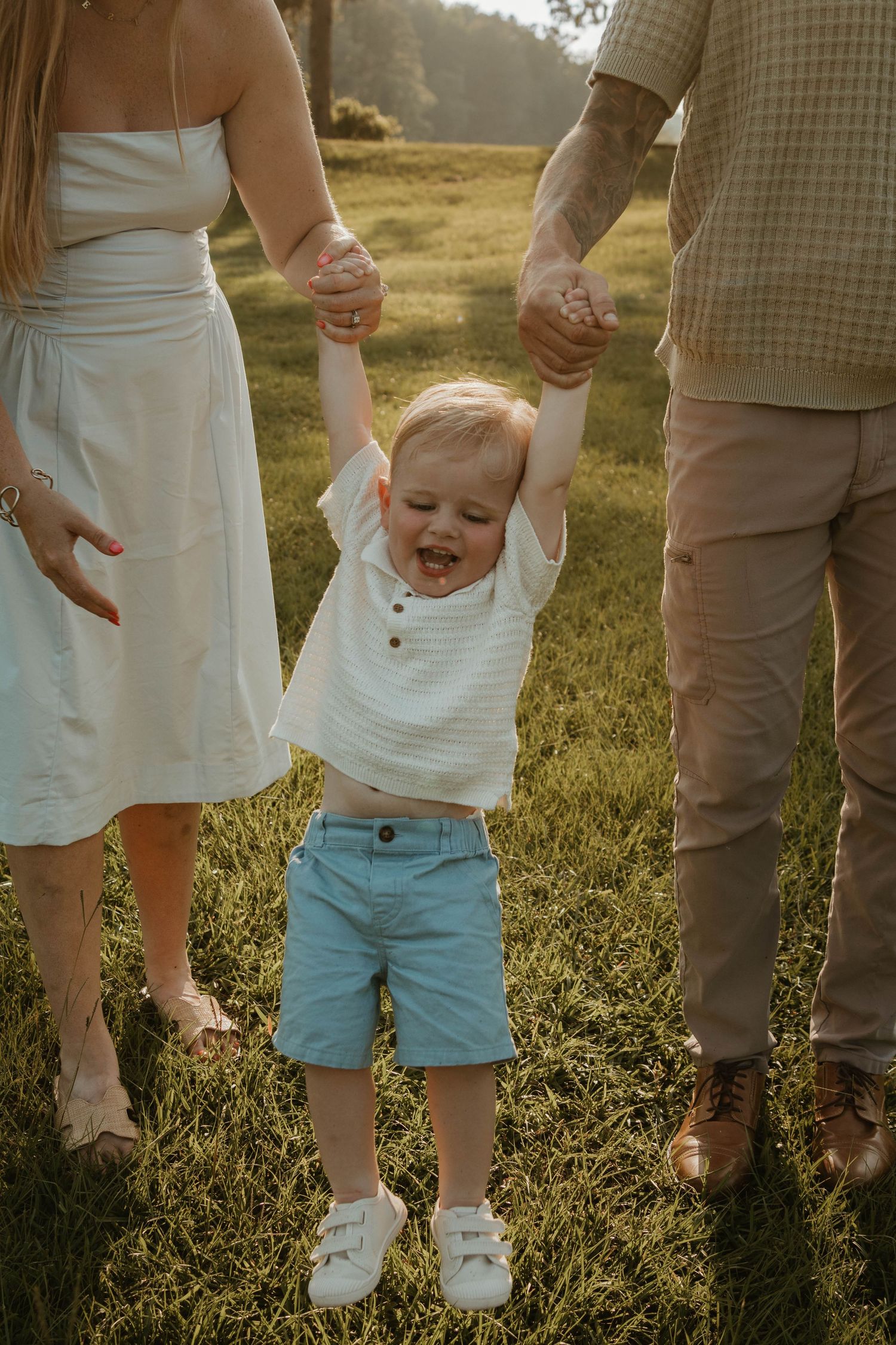 Small child jumps excitedly on grass while wearing blue shorts and white shirt at sunset at The Links in Toccoa, Georgia.