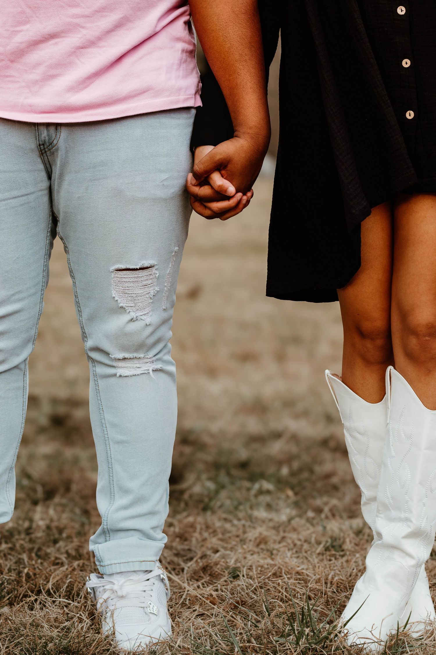 A close-up shot of two people holding hands, showing distressed jeans and white cowboy boots at a venue in northeast Georgia.