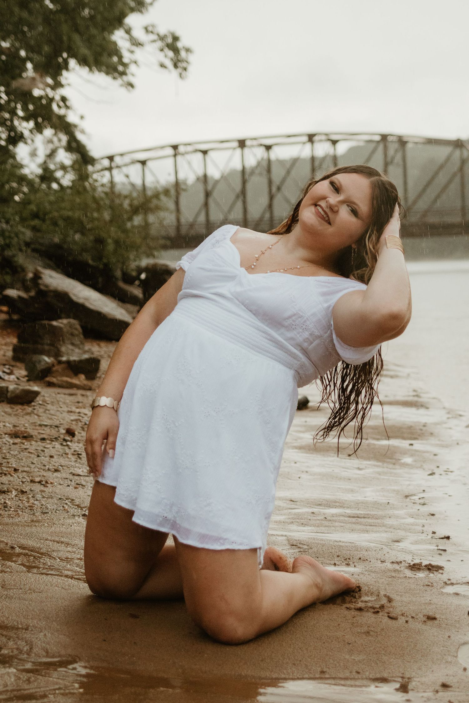Figure in white dress reclines on sandy lake beach during a moody photoshoot by Broken Bridges on Lake Hartwell.