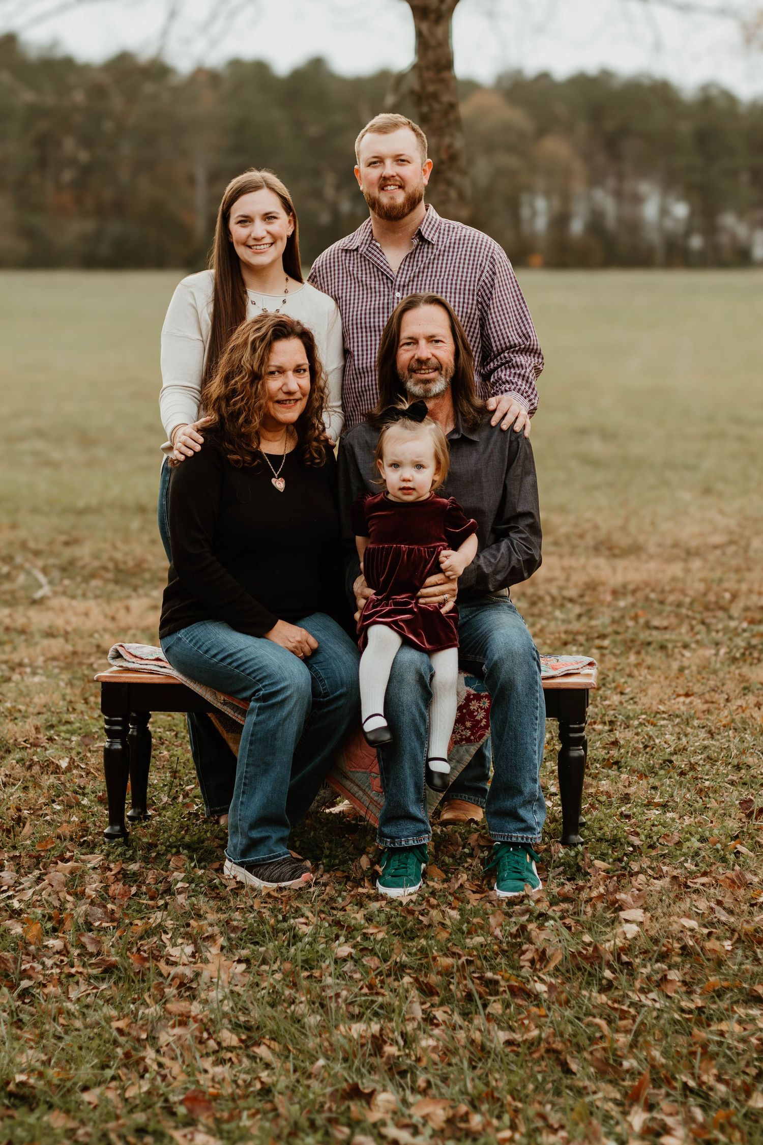 Casual outdoor family portrait session on wooden bench with fall foliage backdrop in Commerce, GA.