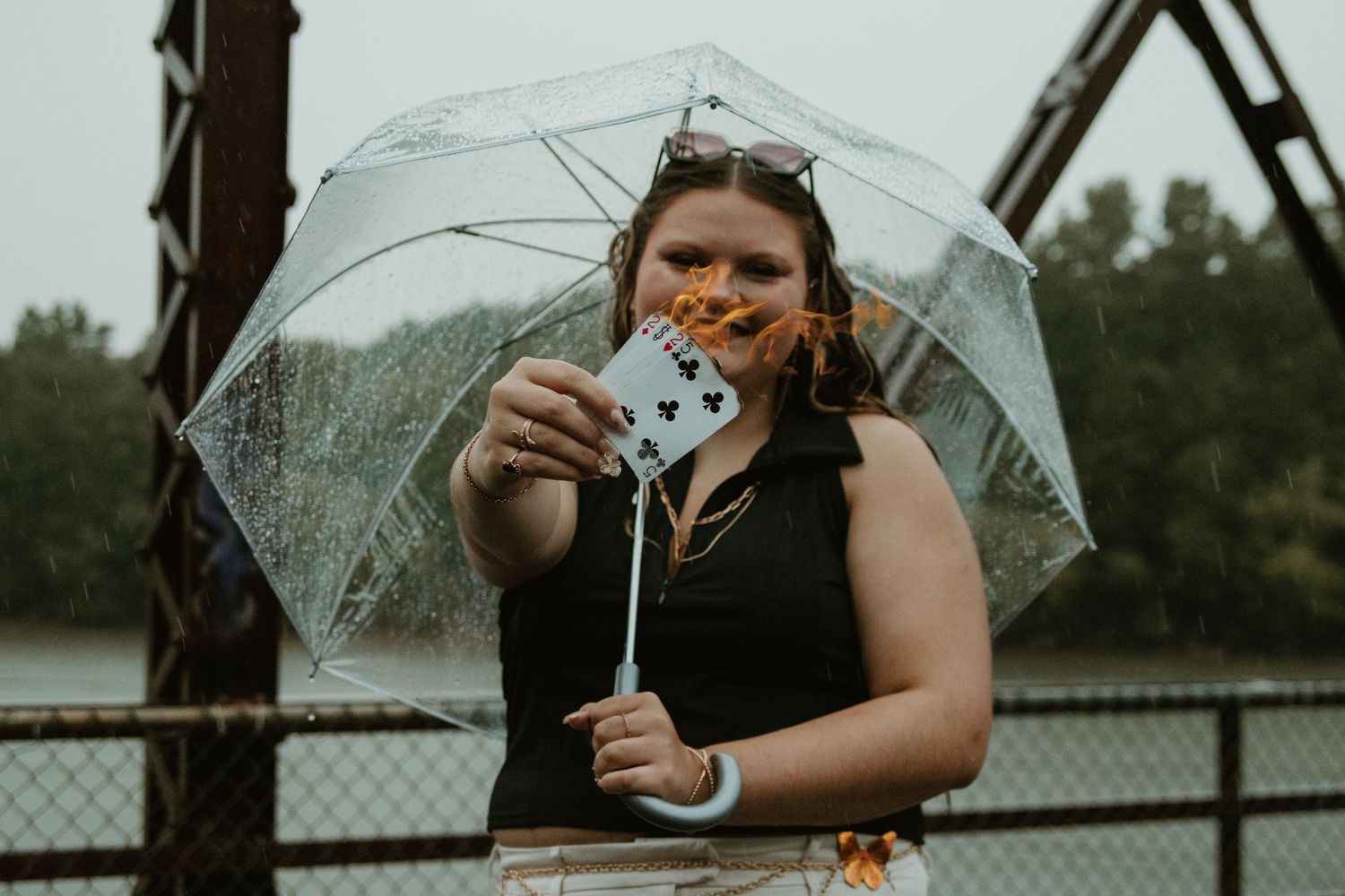 Person holding playing cards while standing under a clear umbrella on a rainy day at Broken Bridges.